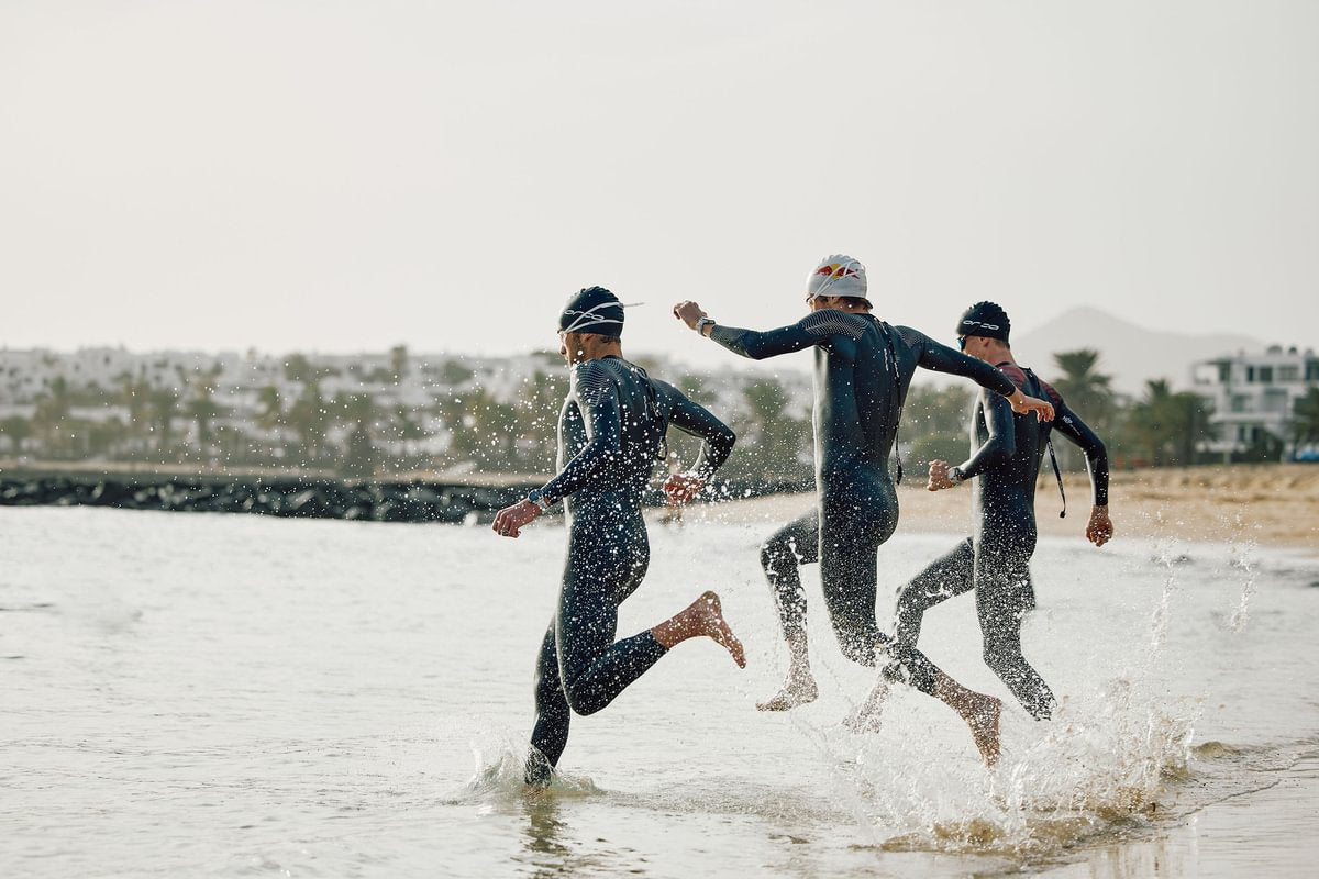 men running into sea wearing black orca wetsuits, goggles and swimhats