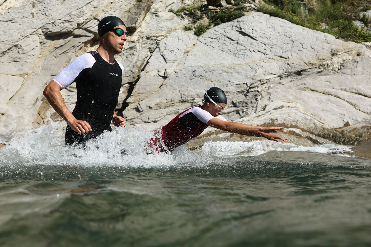 man and woman wearing black and white tri-suits, swimming hats and goggles starting triathlon race with sea swim