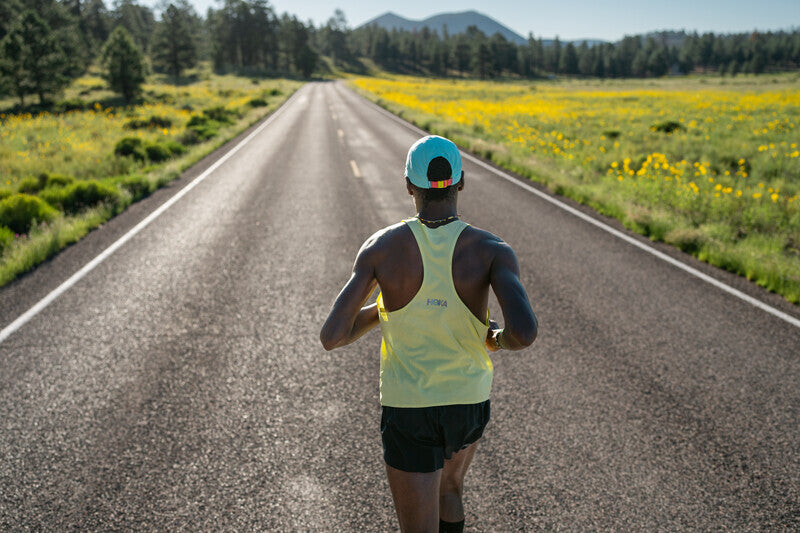 man wearing hoka race day performance singlet in yellow running down country road
