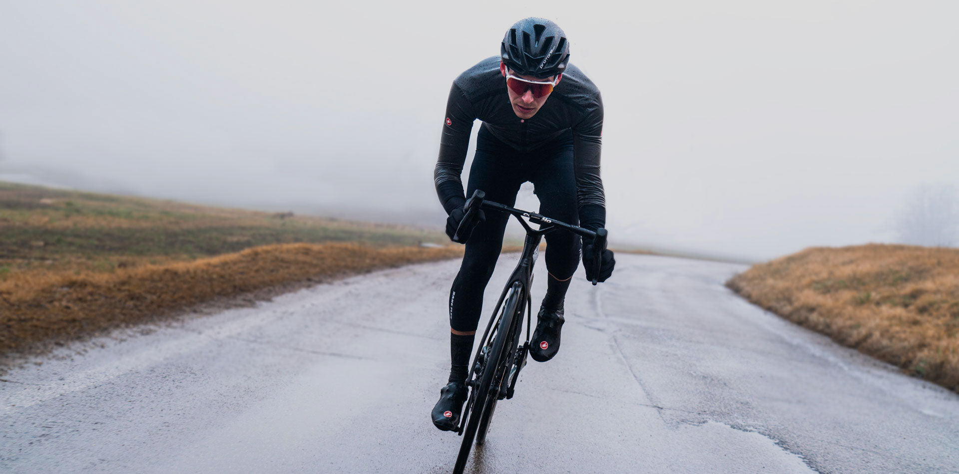 man cycling along wet country road on rainy day wearing waterproof cycling clothing