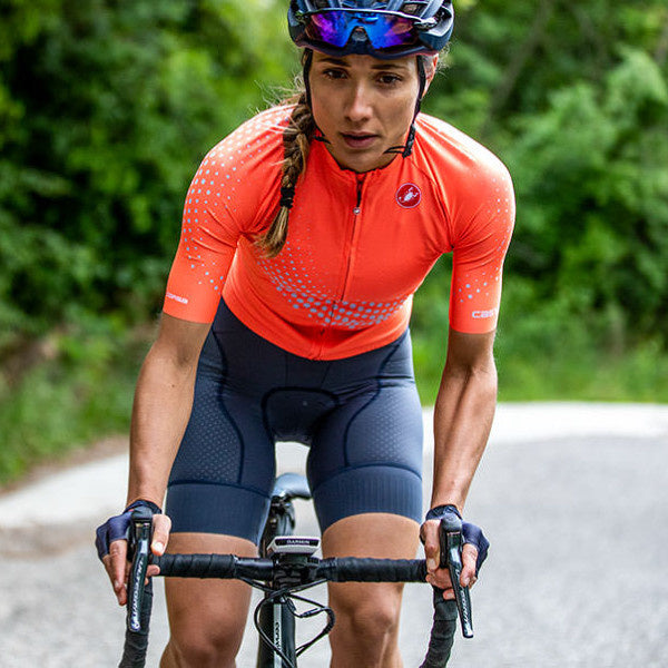 woman cycling on country road wearing orange castelli cycling jersey