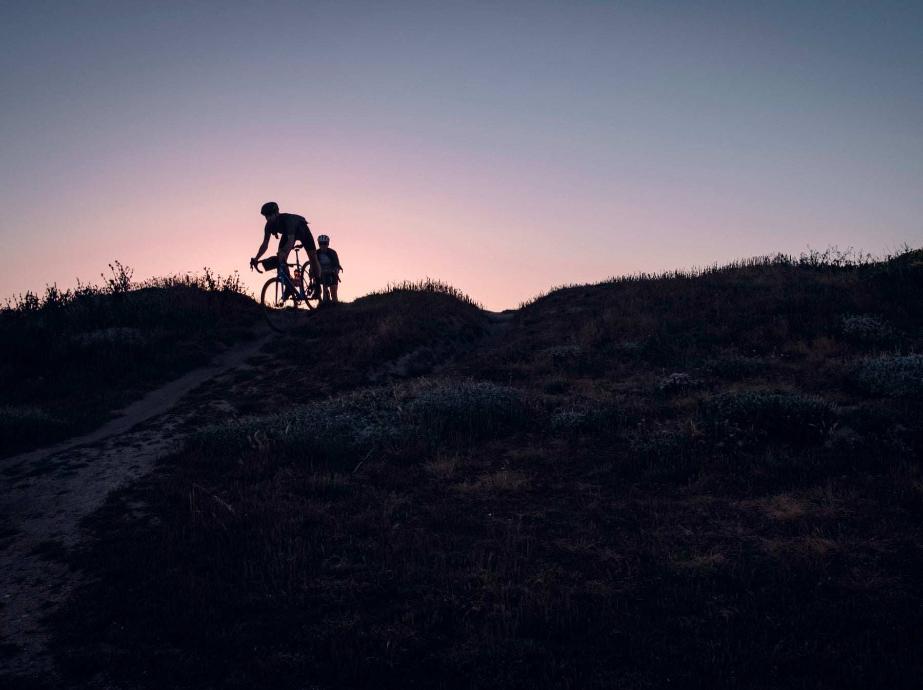 gravel bikes on uneven terrain coming over a hill top silhouetted against the setting sun