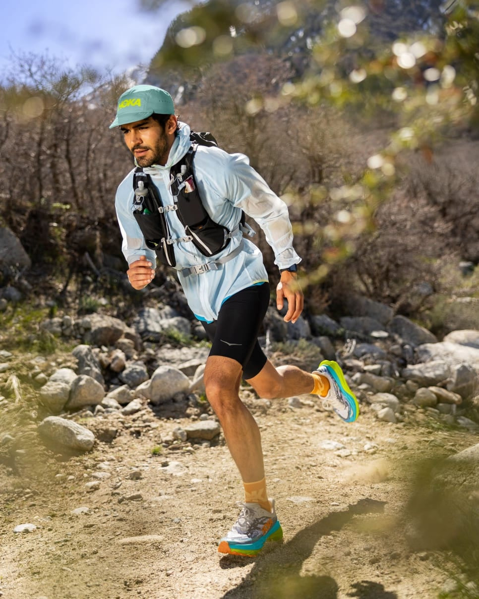man trail running in hoka jacket, with hoka running shoes, hoka shorts, hoka cap