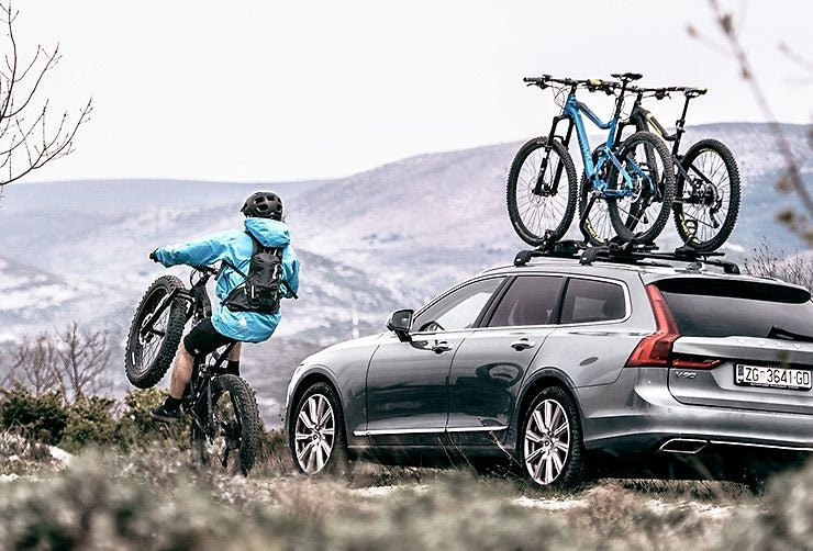 thule bike rack on roof of car travelling through mountains with mountain biker cycling alongside