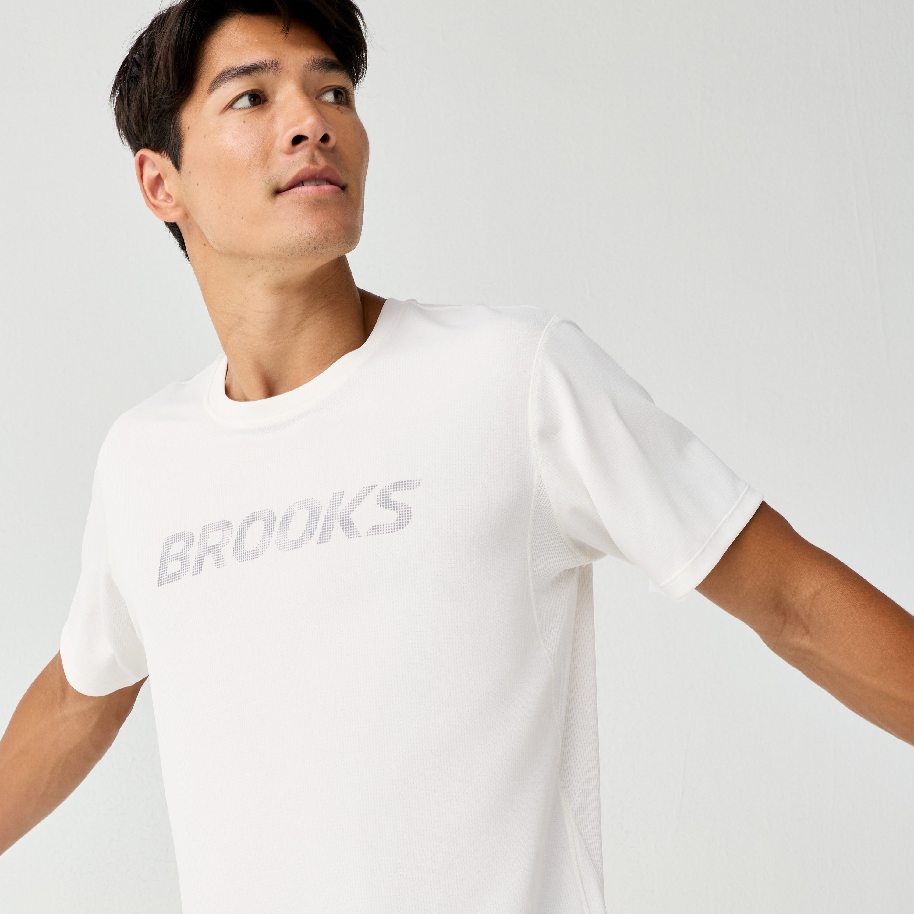 Man wearing Brooks Reflective Dash Tshirt in cream colour with reflective writing