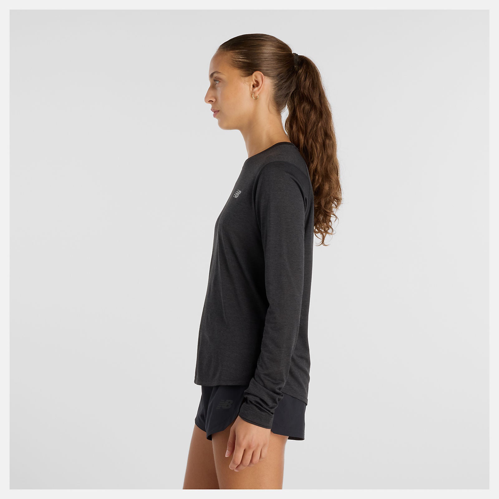 woman wearing NB athletics long sleeve run top in black, showing side with longer length at the back
