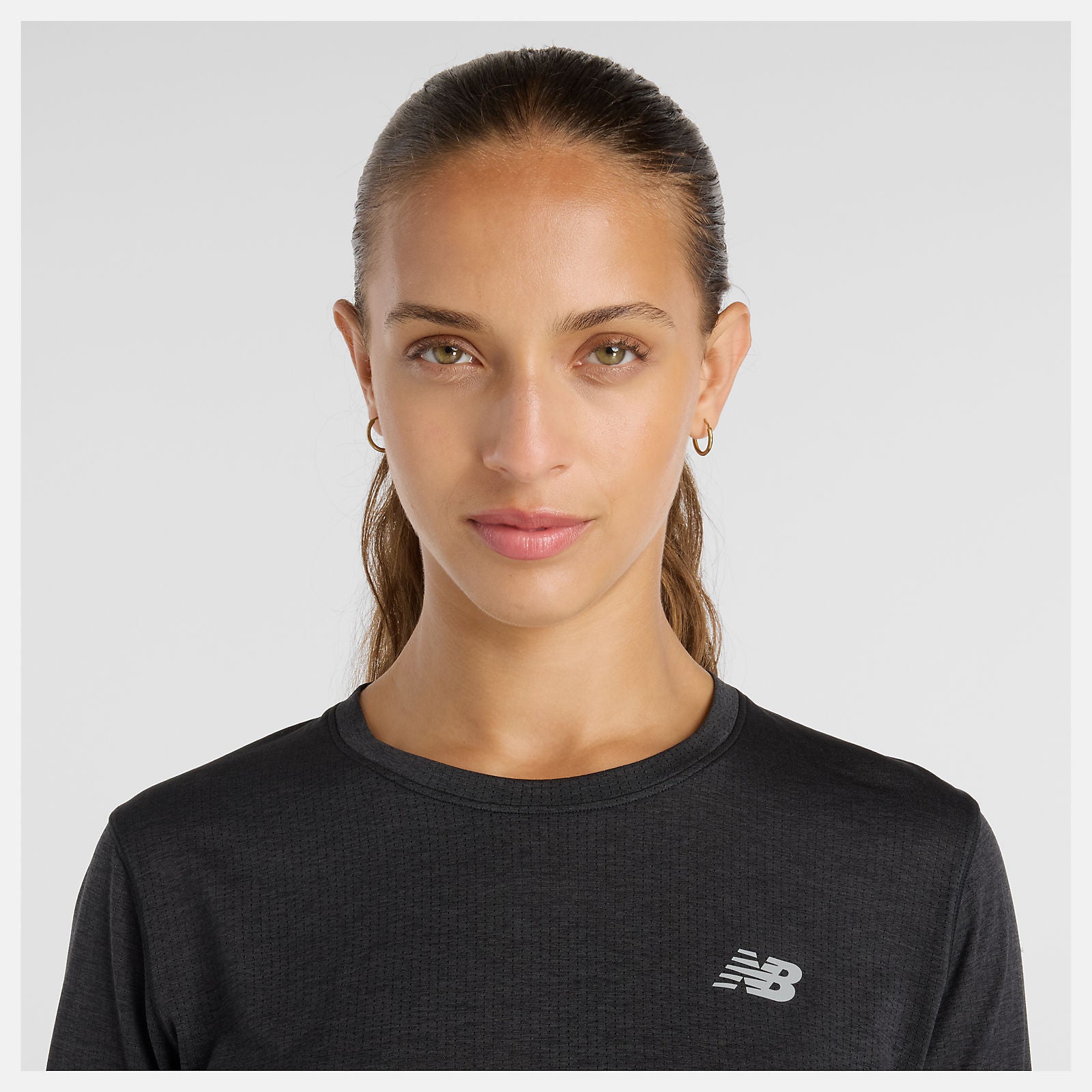close up of woman wearing NB athletics long sleeve run top in black, showing reflective NB logo