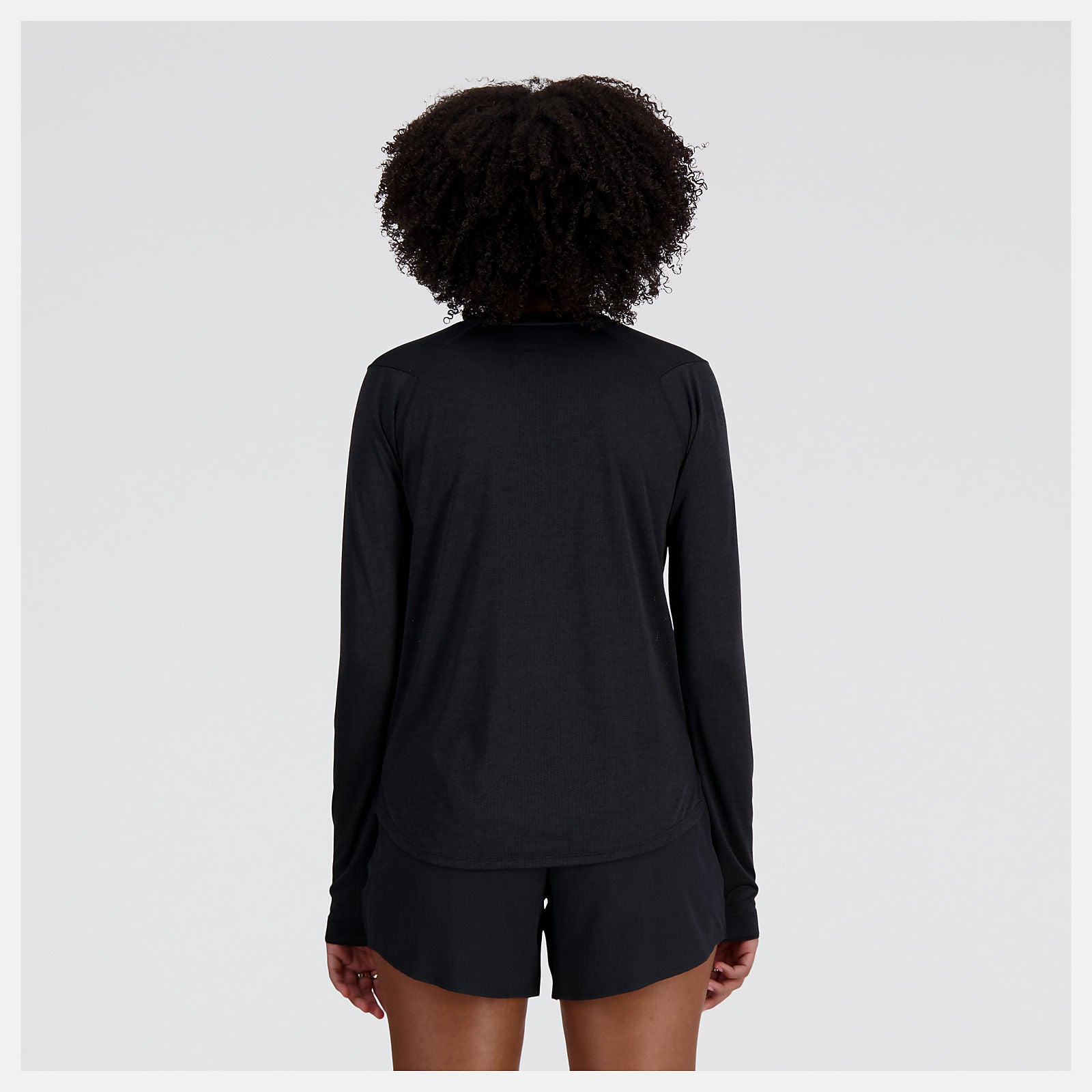woman wearing NB athletics long sleeve run top in black, showing back coverage