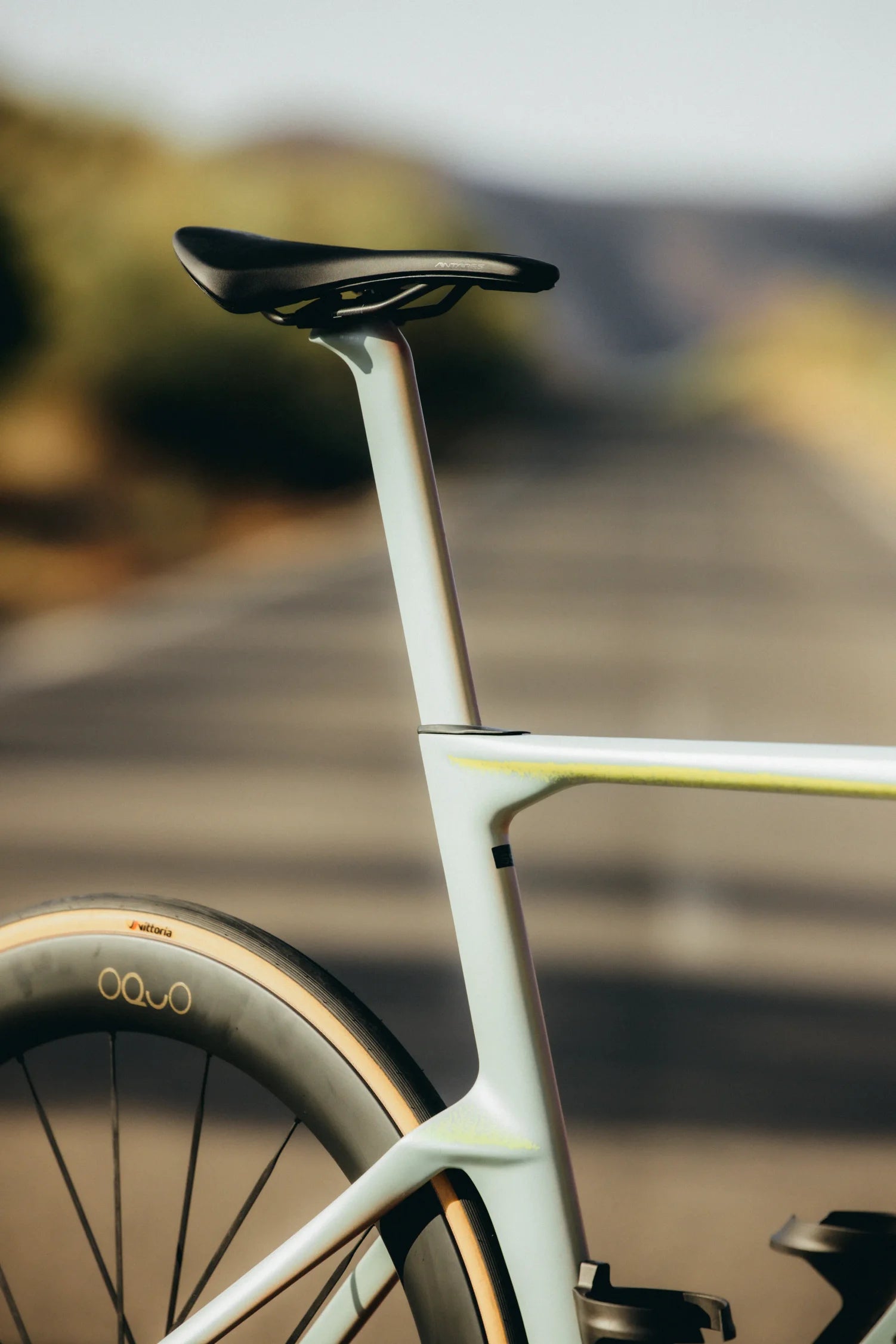 Close-up of an Orbea Aero road bicycle frame and saddle with a blurred outdoor road and hills in the background.