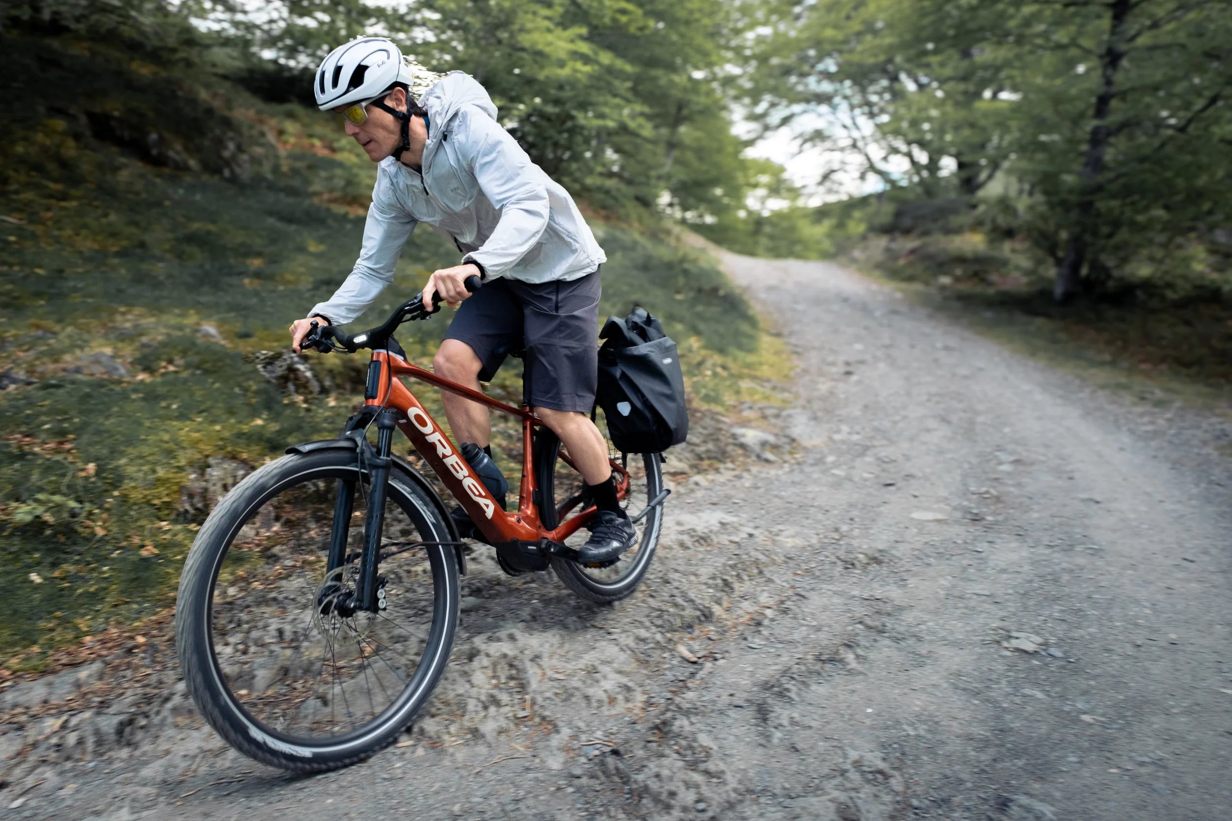 man cycling an orbea kemen electric bike on a gravel road with panniers on the bike