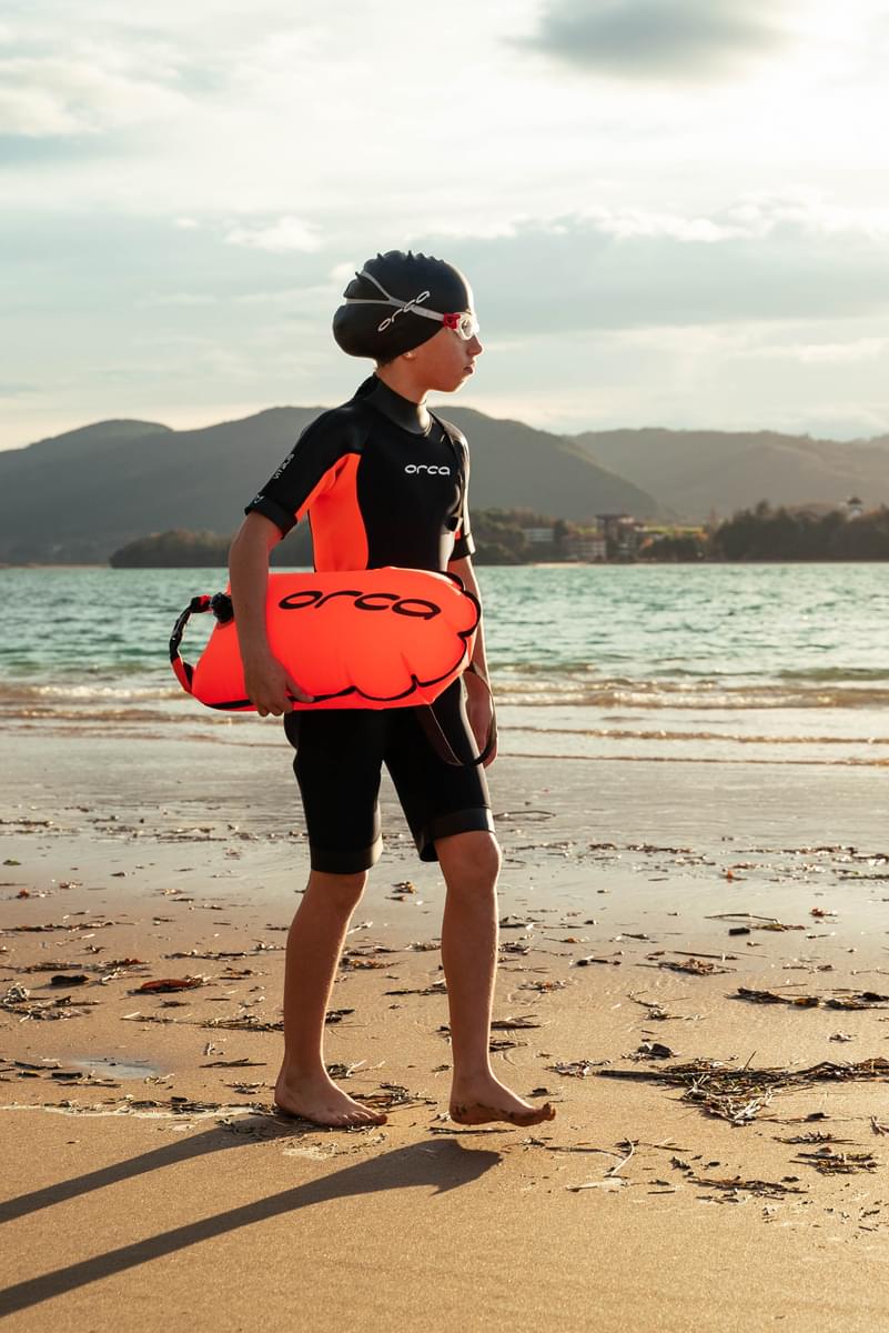 boy sea swimming in Orca junior vitalis shorty wetsuit with orca tow float, orca cap and orca goggles