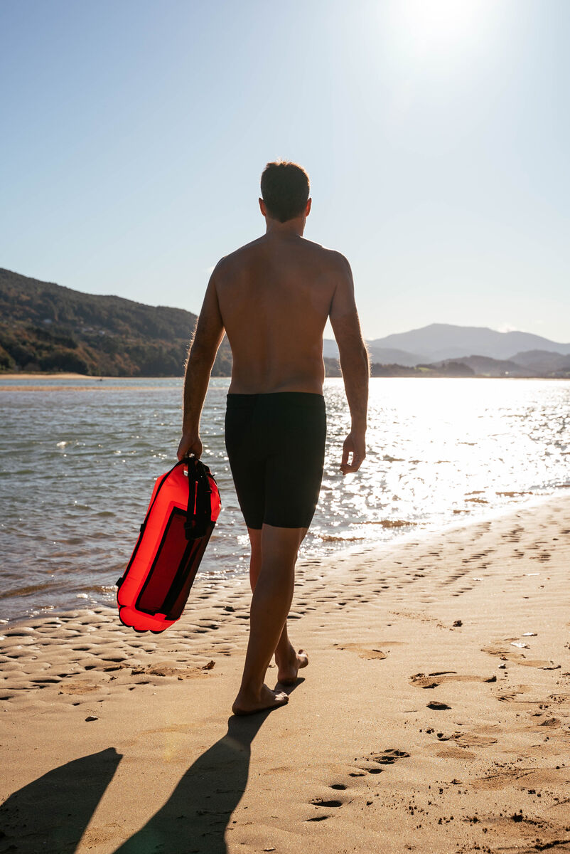 man walking on beach with orca safety buoy with pocket for open water swimming, tow float