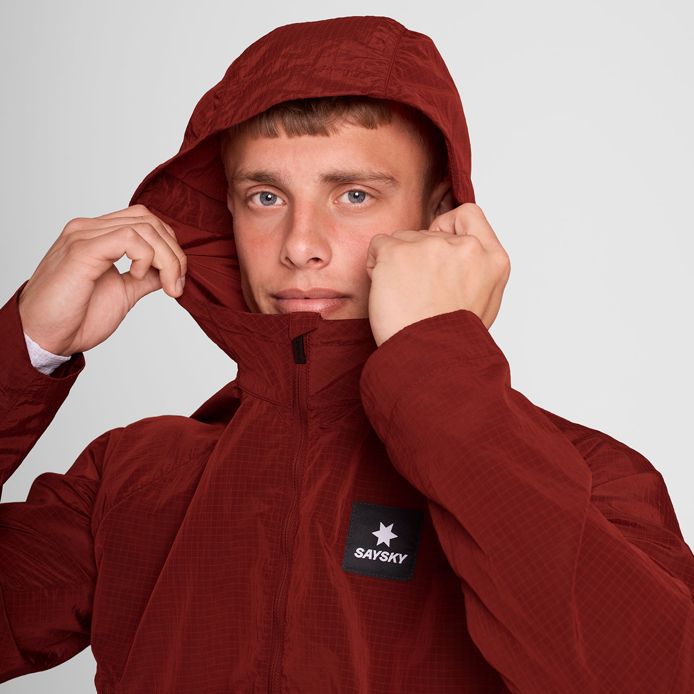 Man wearing SAYSKY clean hooded jacket for road running in red colour showing hood up
