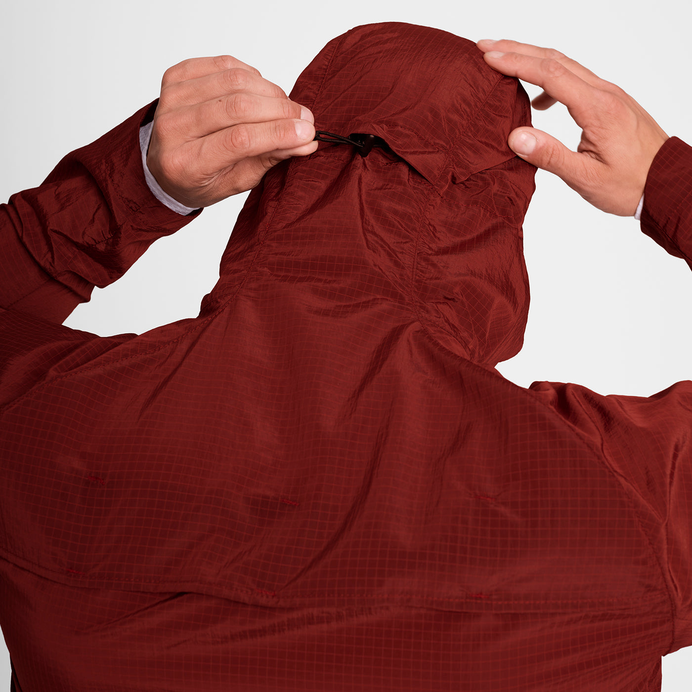 Man wearing SAYSKY clean hooded jacket for road running in red colour, showing toggle feature on hood for windy days