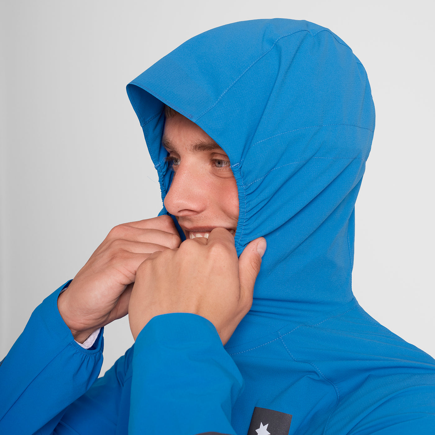 Man wearing SAYSKY Clean Pace Flex Hooded Running Jacket in blue, showing elasticated hood