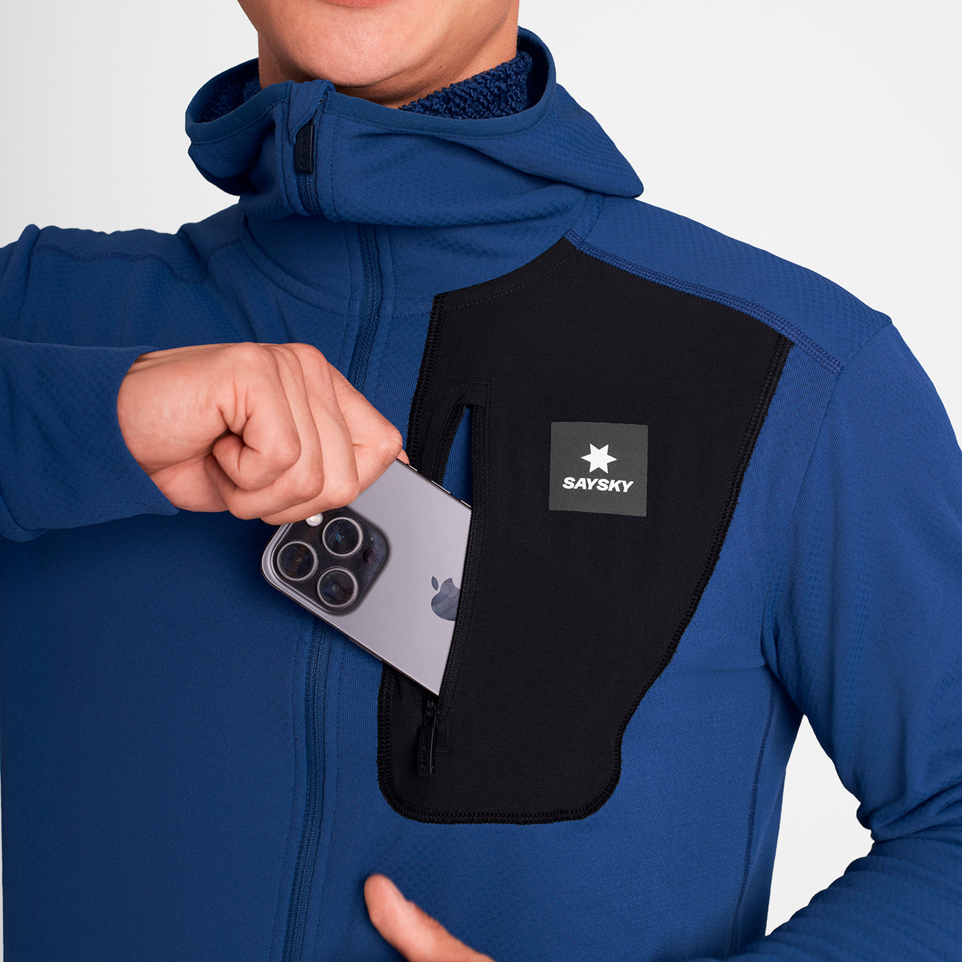 man wearing SAYSKY long sleeve, blue and black, fleece run top, showing pocket that stores phone
