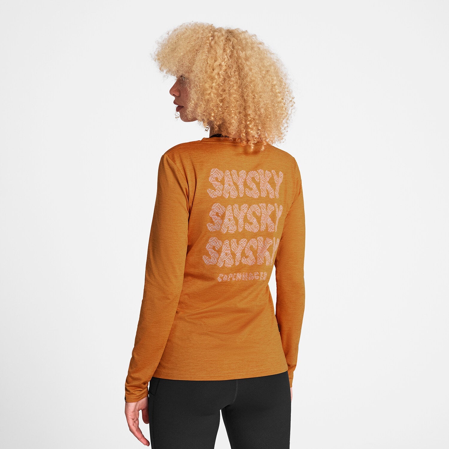 Woman wearing orange SAYSKY long sleeve Pace run top, showing the text on the back