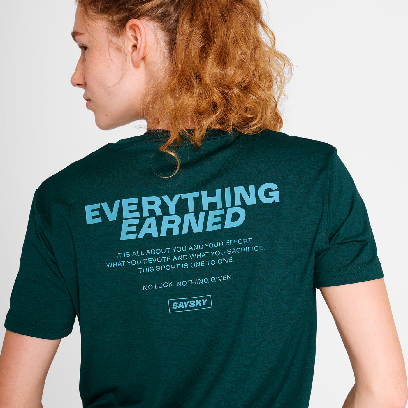 Woman wearing a green SAYSKY running t-shirt with 'EVERYTHING EARNED' text on the back