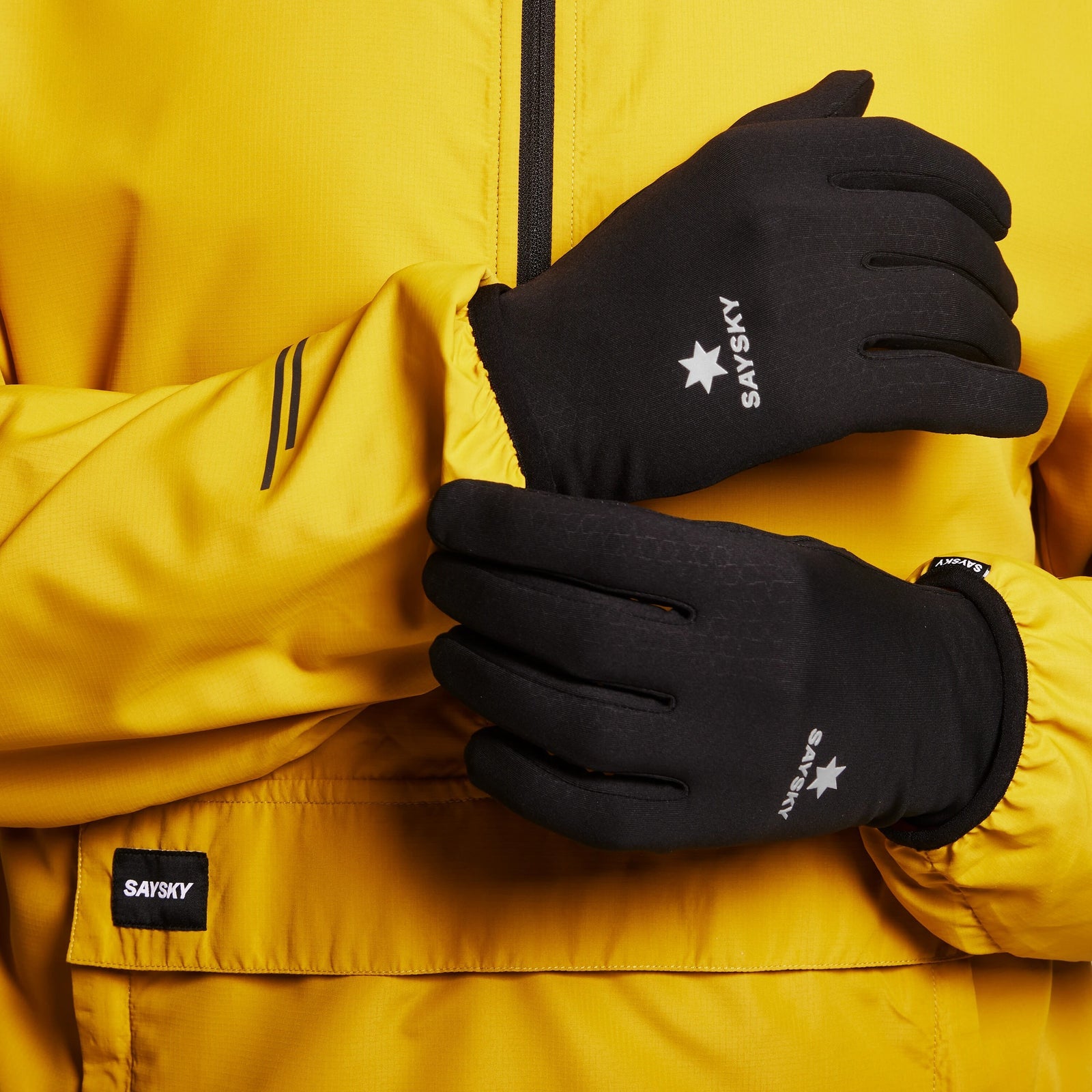 Model wearing pair of black unisex saysky thermal combat gloves with yellow saysky jacket 