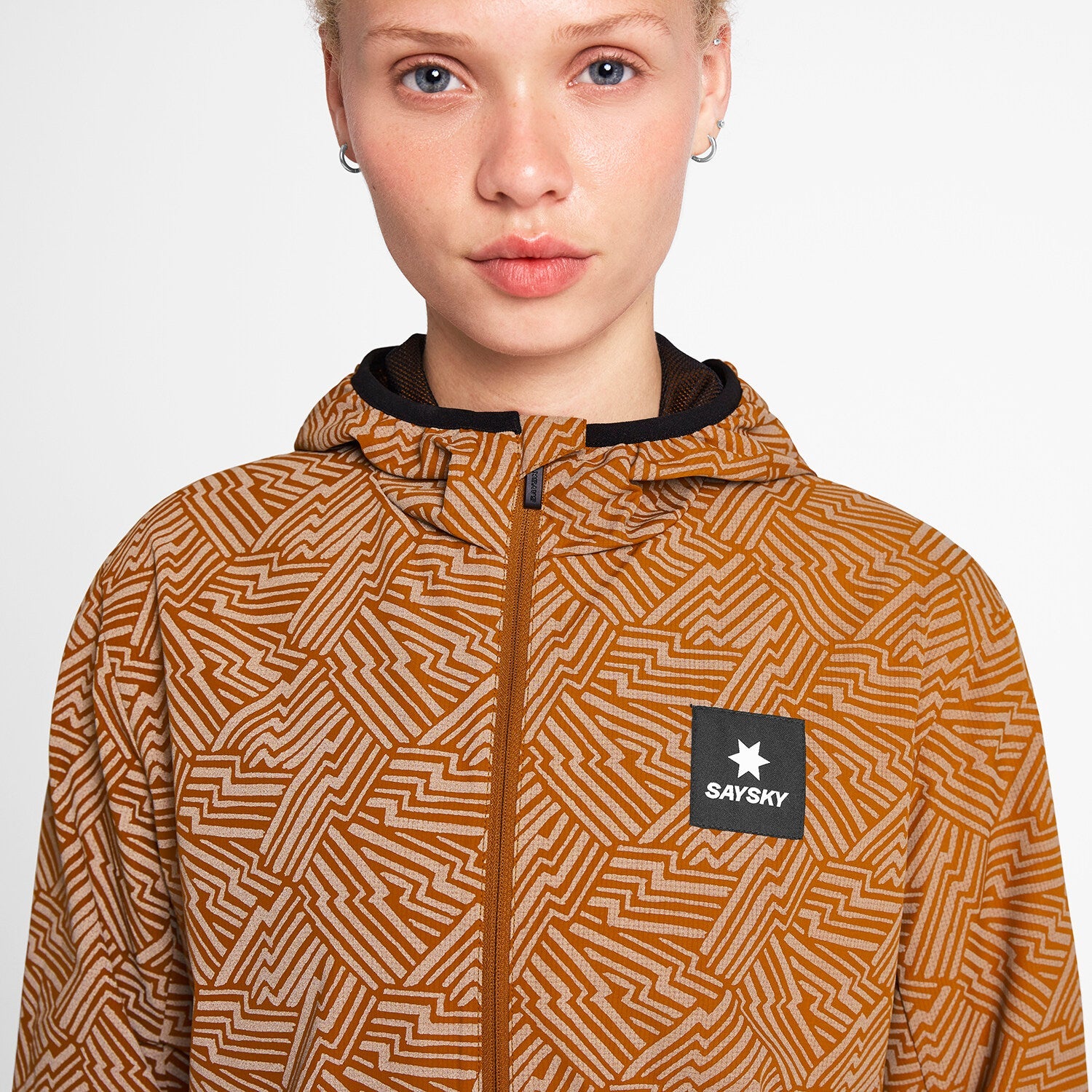 Woman wearing SAYSKY reflective blaze jacket in orange colour, showing close up of zip, logo and fabric