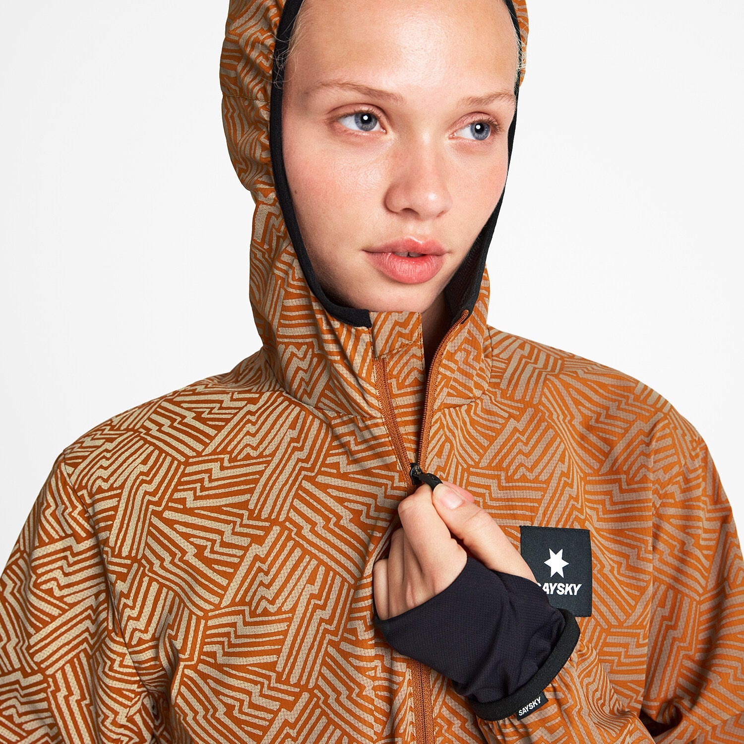 Woman wearing SAYSKY reflective blaze jacket in orange colour, with hood up