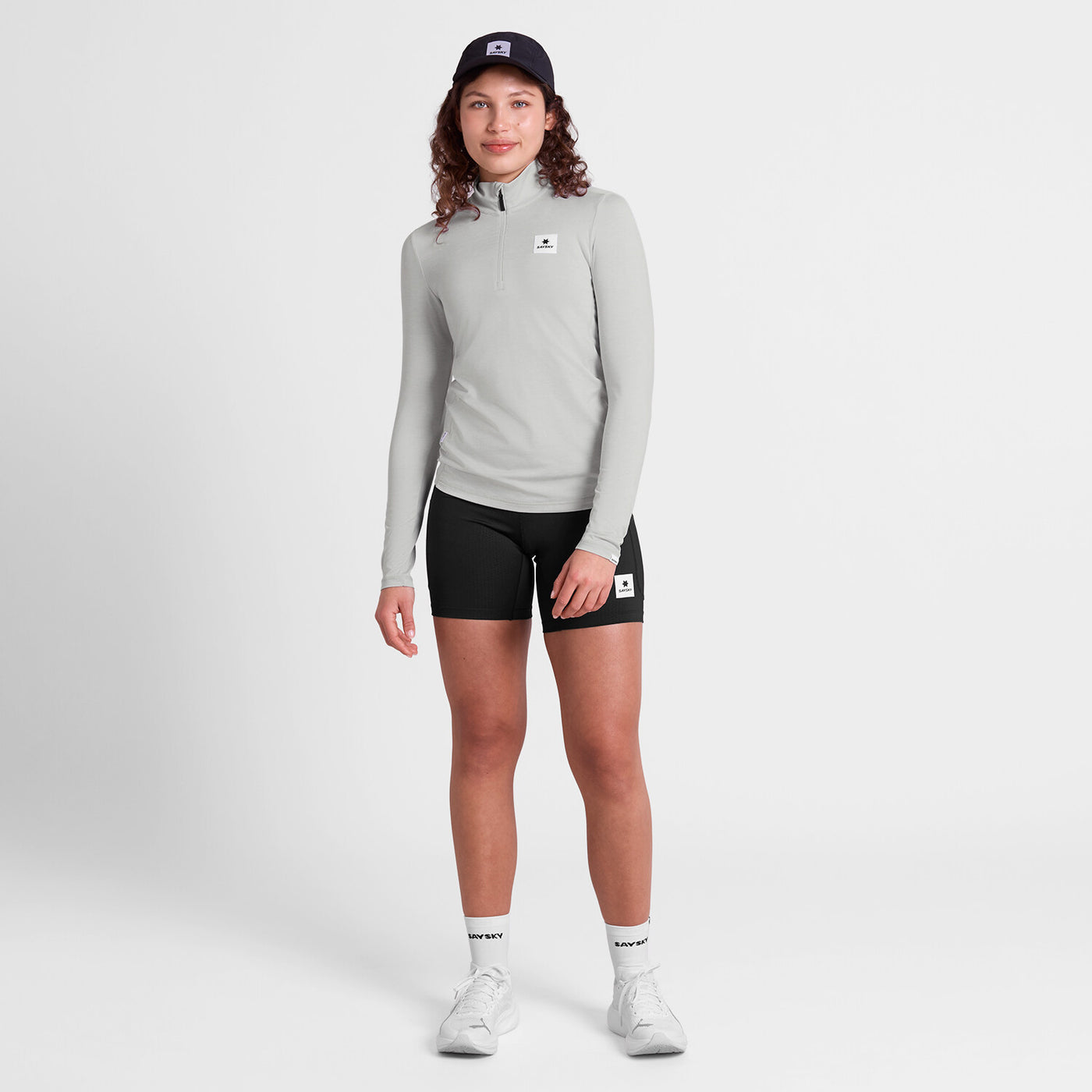 saysky womens pace 1/2 zip long sleeve, lightweight breathable half zip top for running, light grey colour, full body shot of woman wearing grey saysky top and black shorts