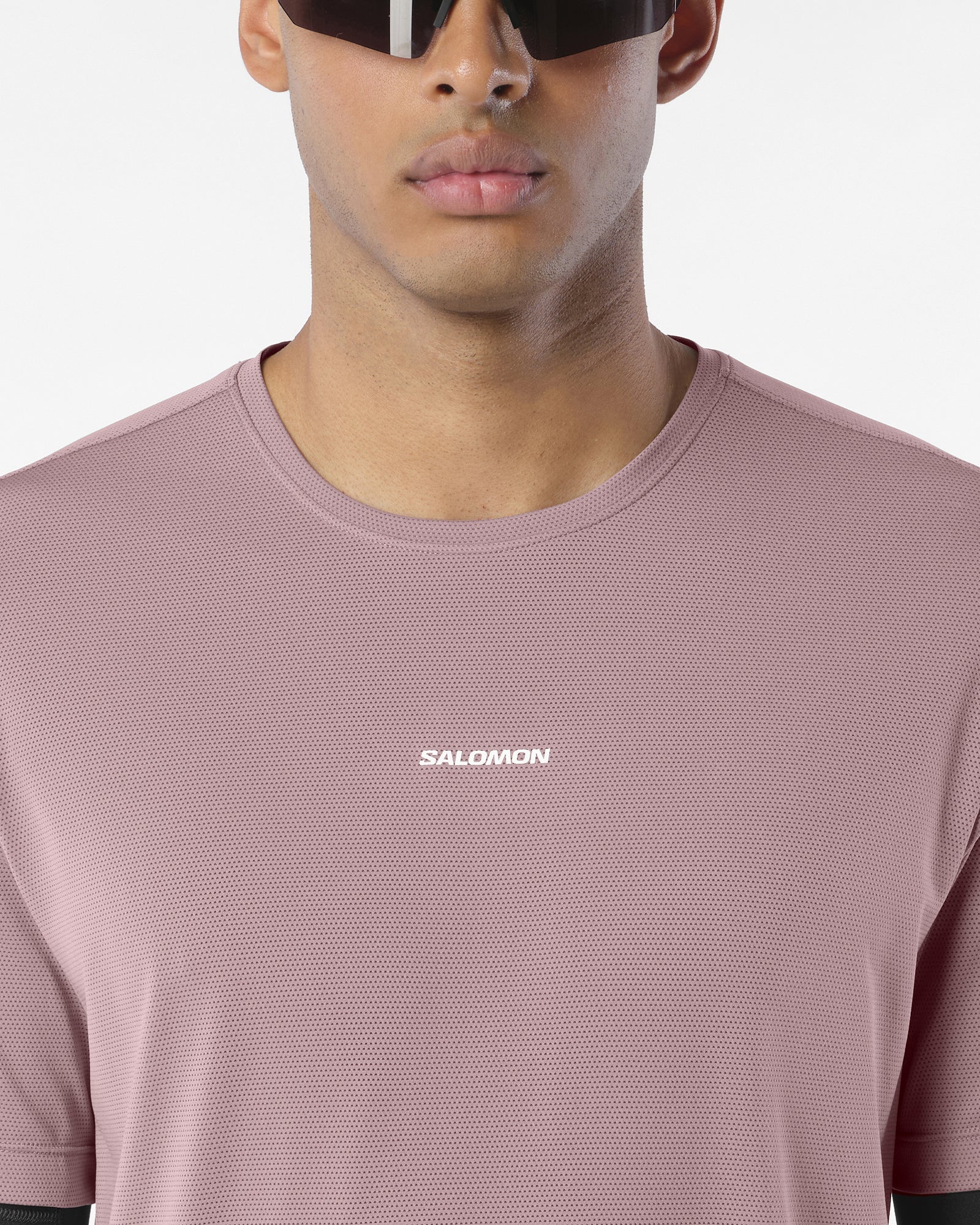 Close up of a an wearing salomon shakeout core tee in a pink colour, reflective logo on front