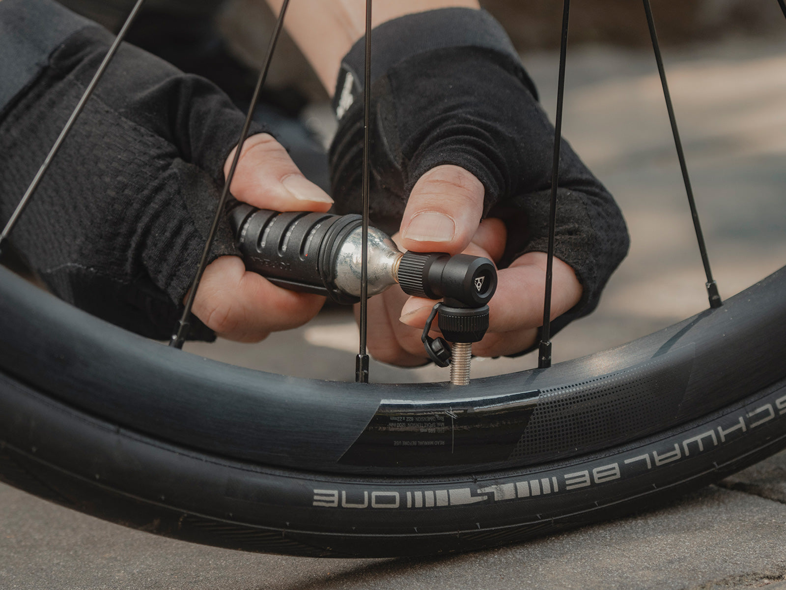 Person inflating a bicycle tire with a topeak nano airbooster pump, focusing on the hands and tool.