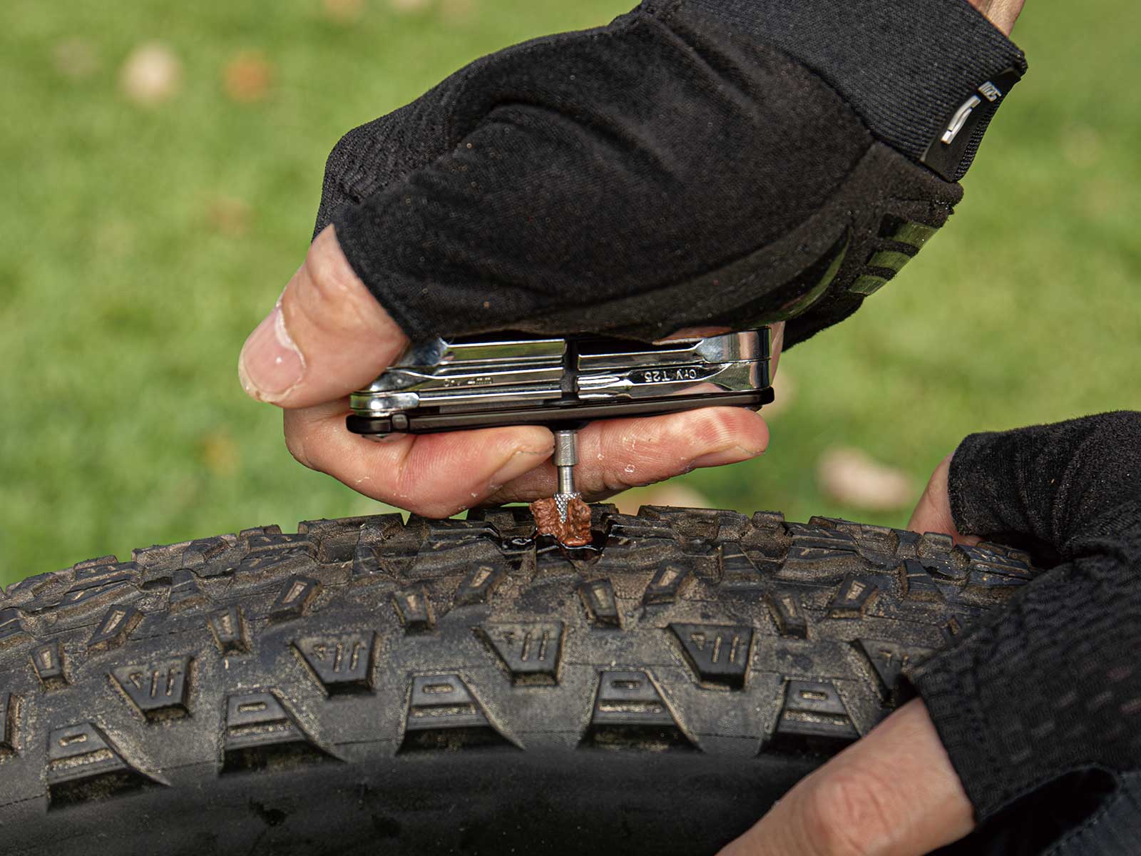 topeak tubi 11 functions multitool with tubeless puncture repair, black with silver tools, hand using tool to patch tyre puncture