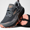 brooks cascadia 20 for women, road to trail gravel running and walking shoe, dark grey and black with peach detail, one shoe tipped over with one shoe sitting lifted on top with untied laces