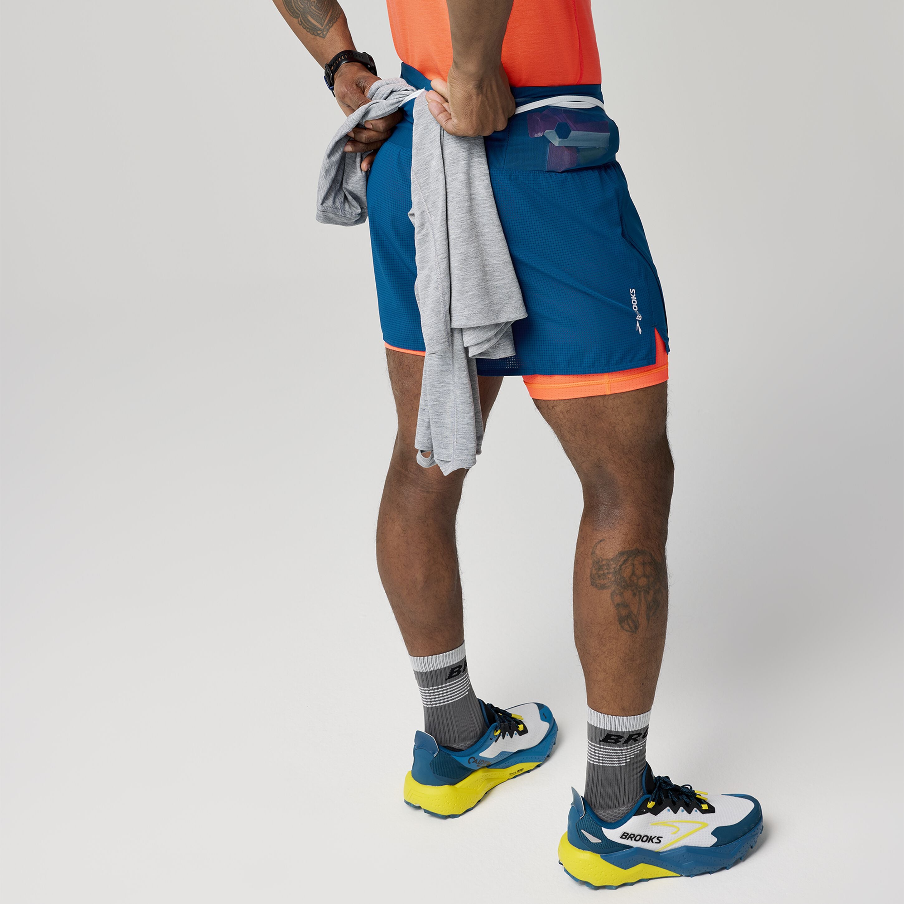 Man wearing Brooks High Point 2in1 trail shorts for men blue and orange colour showing how to use belt pockets