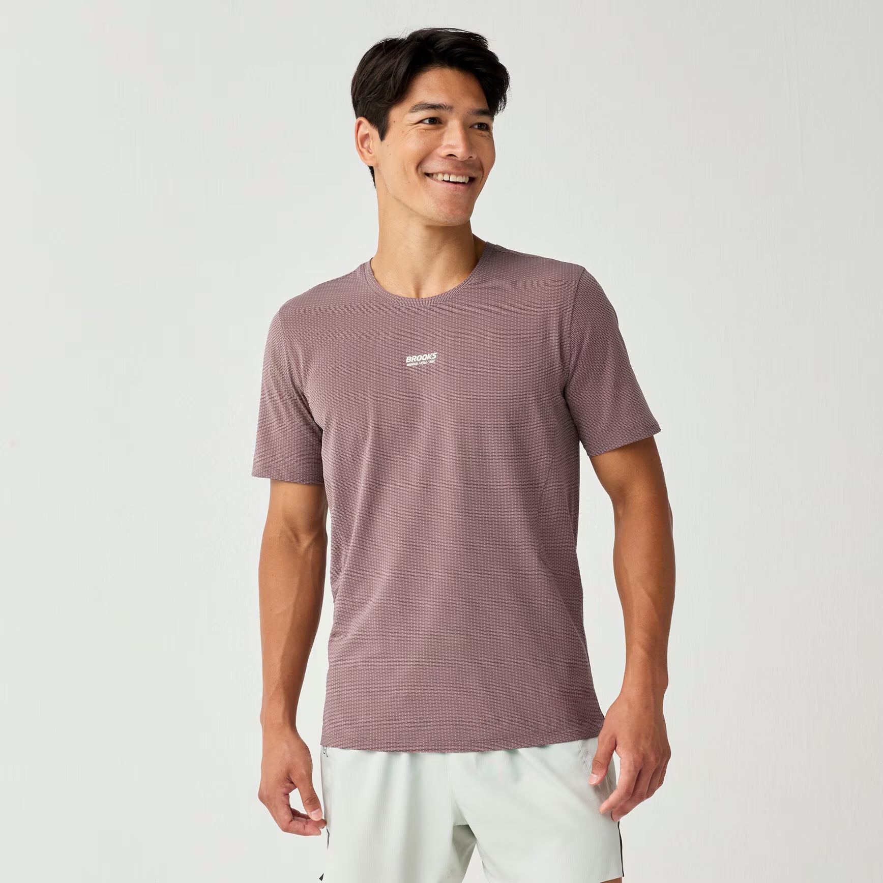 brooks high point short sleeve 2.0 for men, super lightweight and breathable trail running top, purple colour, man wearing brooks top with grey background