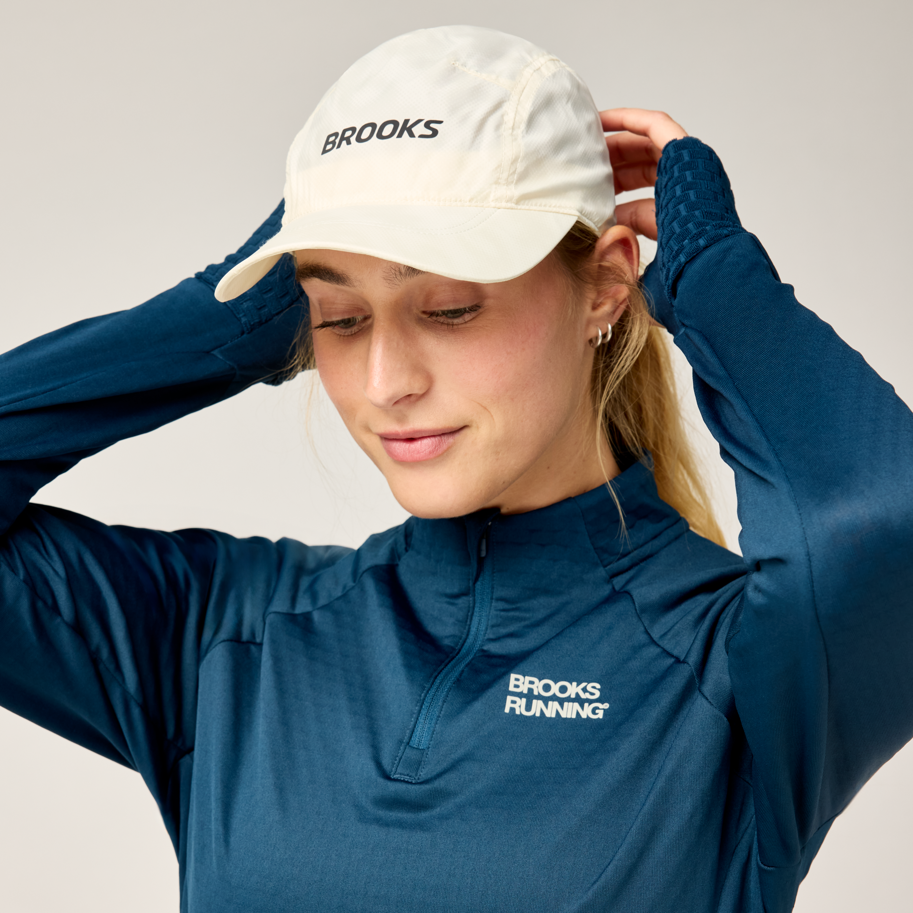 brooks journey reflective hat, lightweight sweat wicking reflective running hat, white colour with reflective silver logo, woman wearing running hat