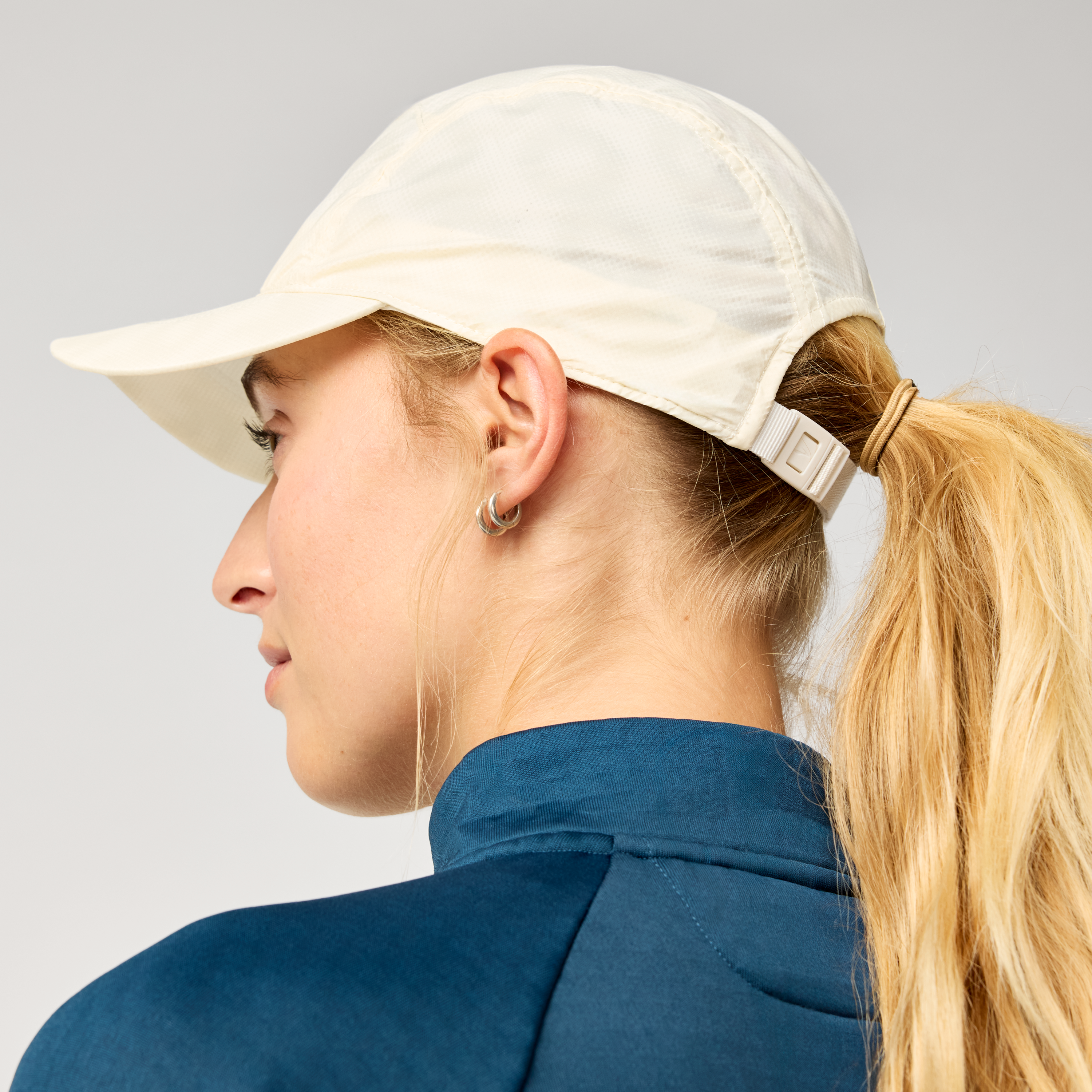 brooks journey reflective hat, lightweight sweat wicking reflective running hat, white colour with reflective silver logo, back of woman wearing running hat with pony tail 