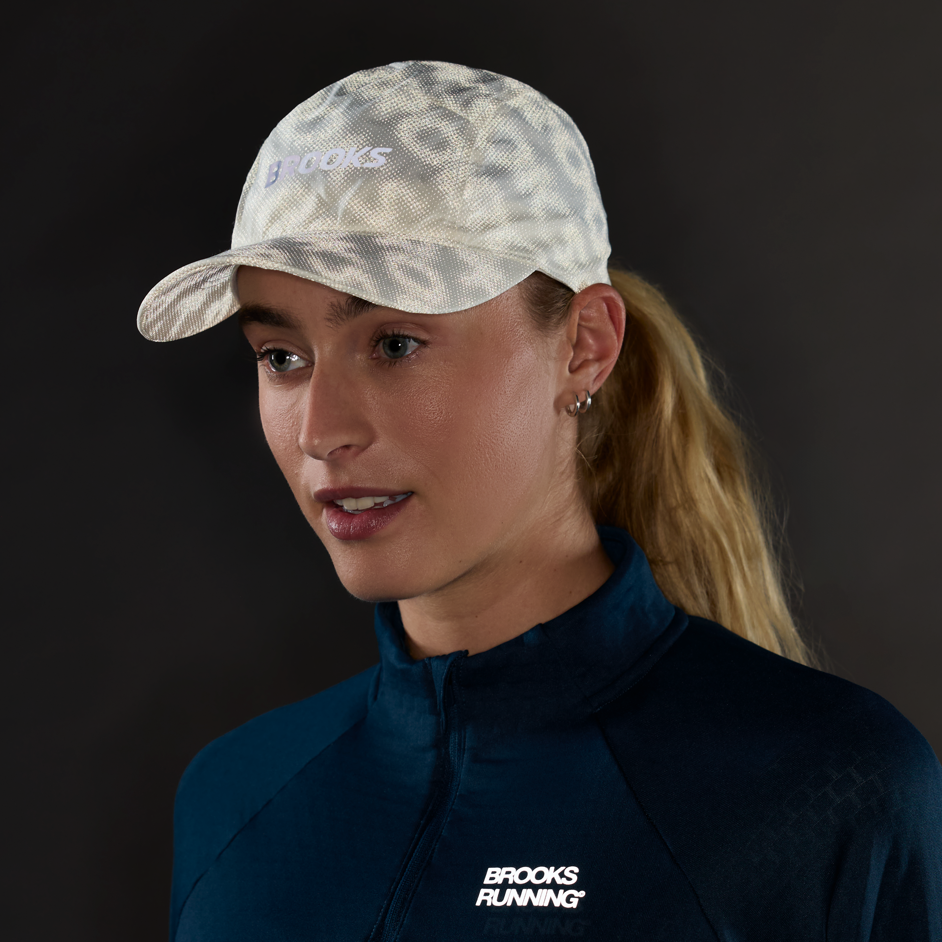 brooks journey reflective hat, lightweight sweat wicking reflective running hat, white colour with reflective silver logo, woman wearing running hat in dark with reflective hat pattern