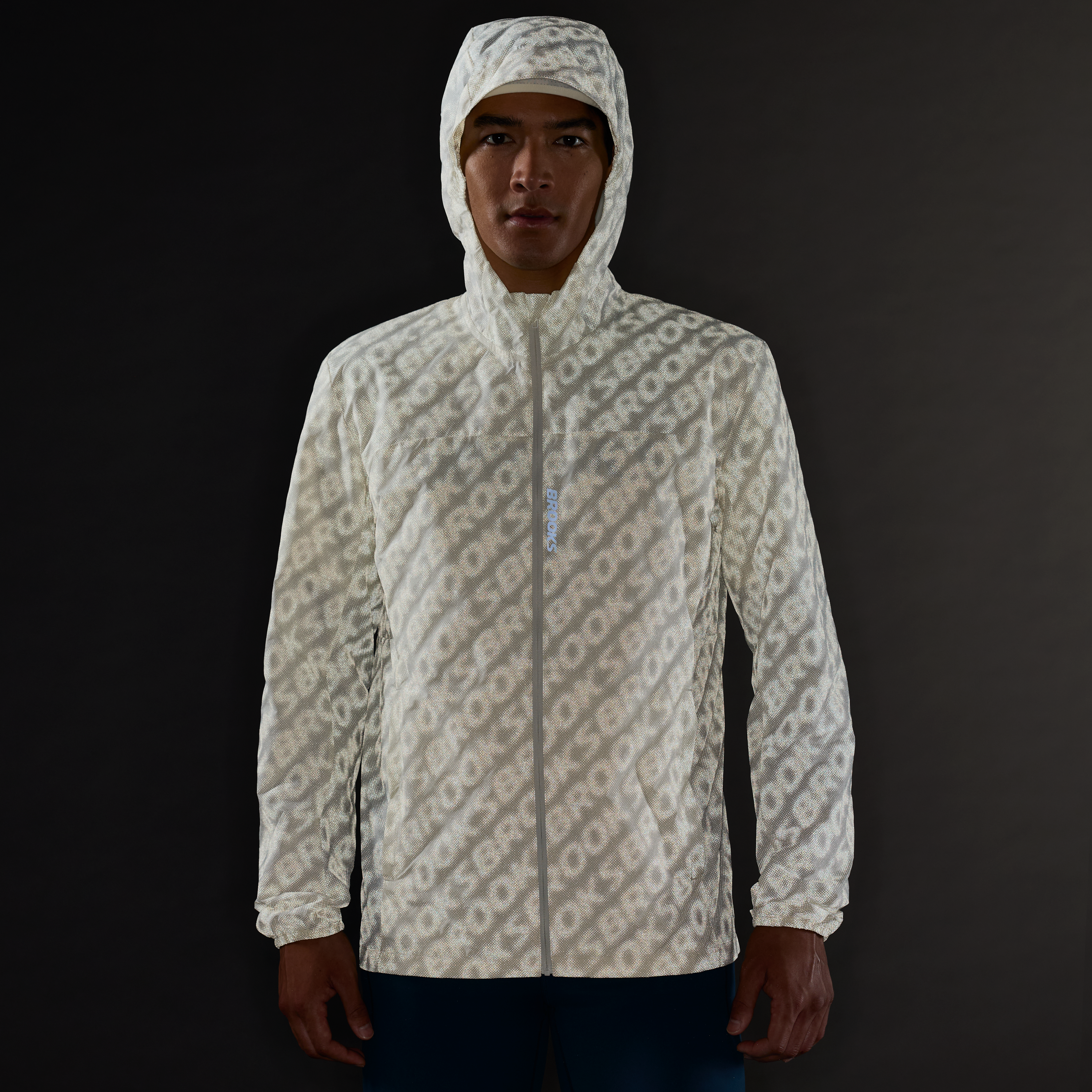 Man wearing Brooks Canopy Reflective Run Jacket, white colour, reflective details, showing the way the jacket reflects in the dark