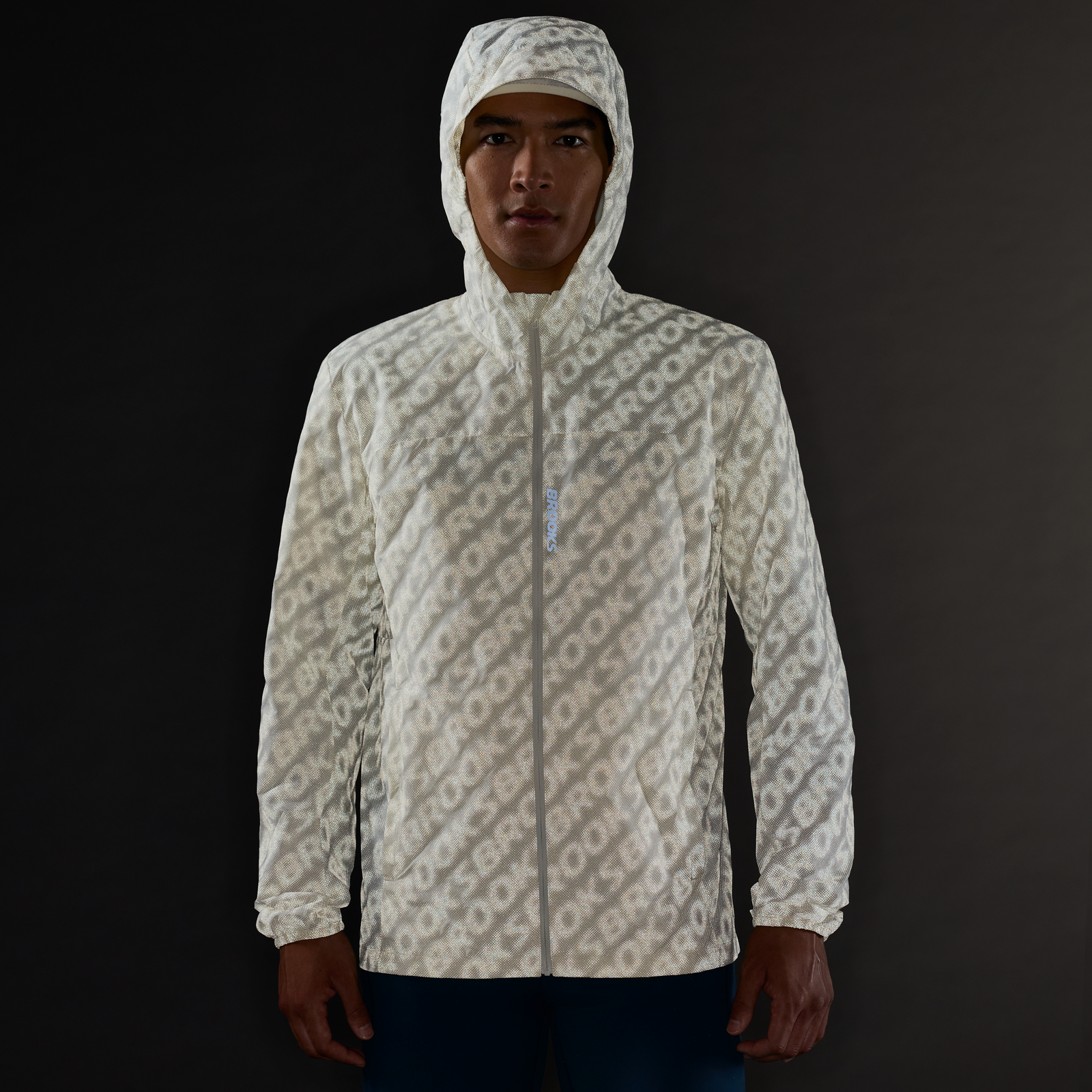 Man wearing Brooks Canopy Reflective Run Jacket, white colour, reflective details, showing the way the jacket reflects in the dark