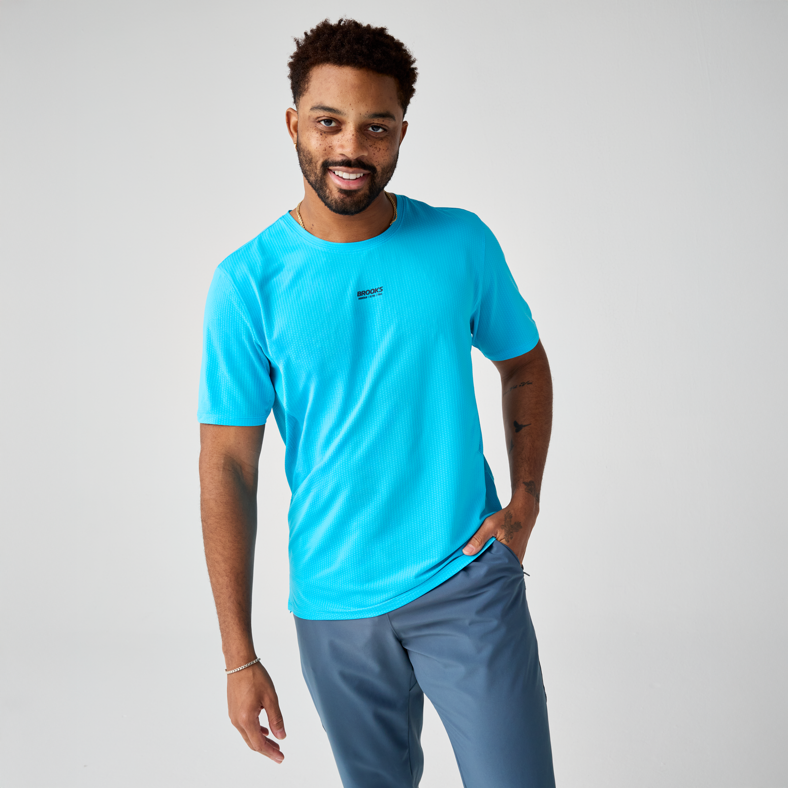 brooks high point short sleeve 2.0 for men, super lightweight and breathable trail running top, bright blue colour, man wearing brooks top with grey background