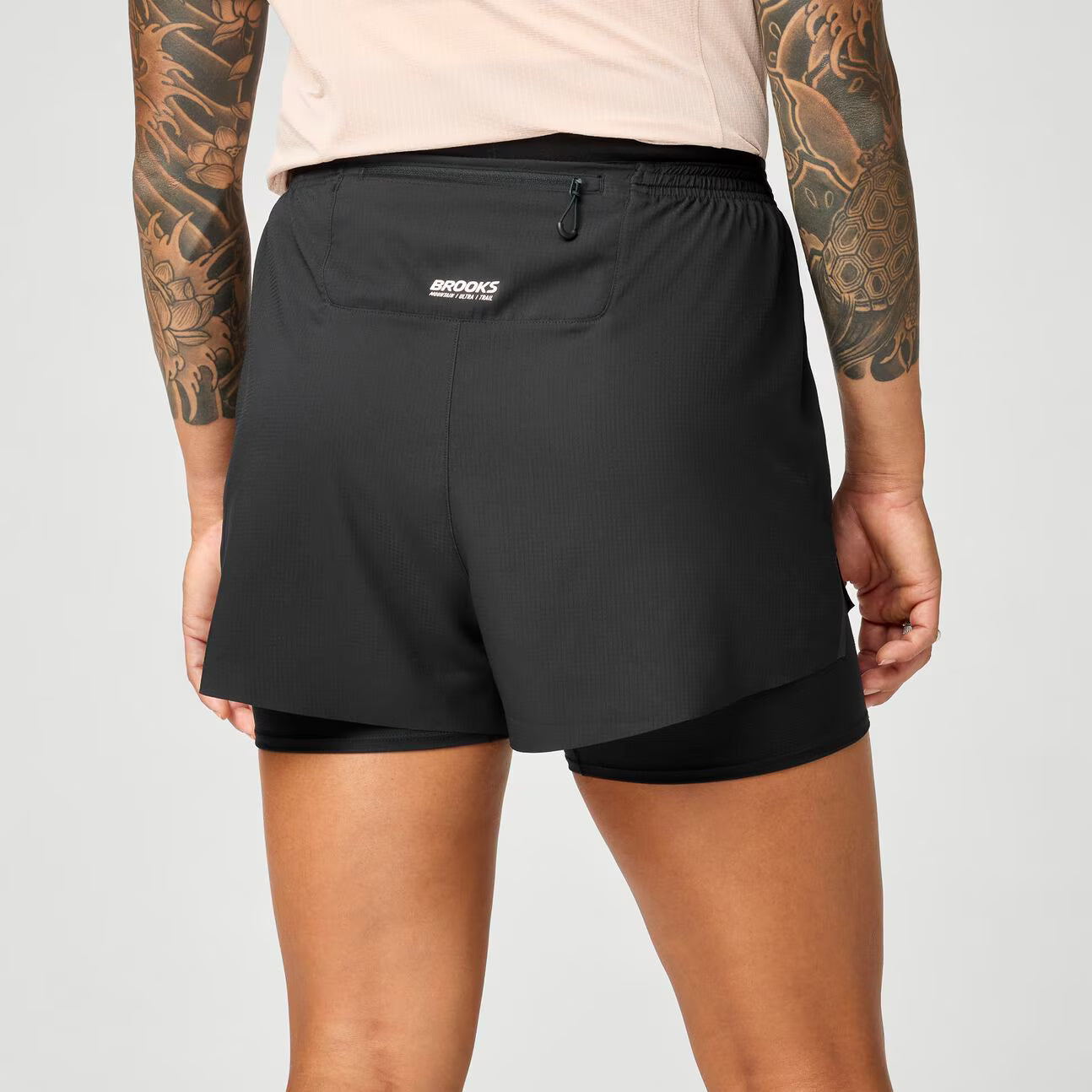 brooks cascadia 2-in-1 short, lightweight running short with pockets for women, black colour with white brooks logo, back view of woman wearing brooks shorts on a white background