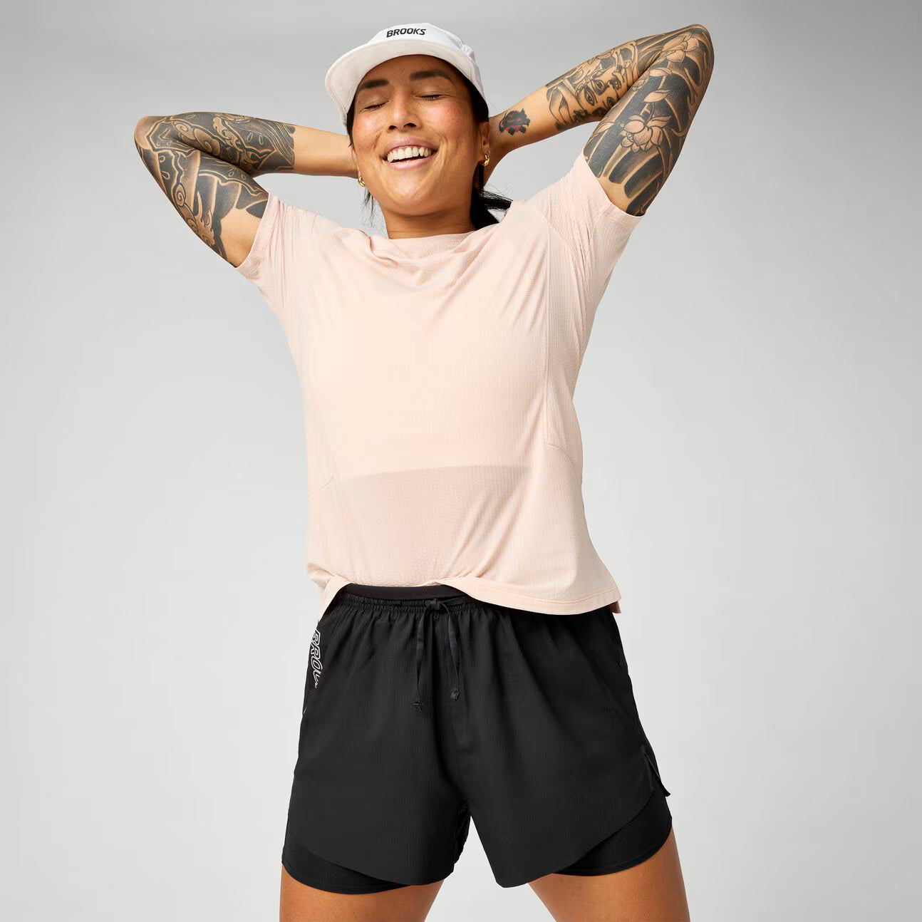 brooks cascadia 2-in-1 short, lightweight running short with pockets for women, black colour with white brooks logo, view of woman wearing brooks shorts and a pink t-shirt on a white background