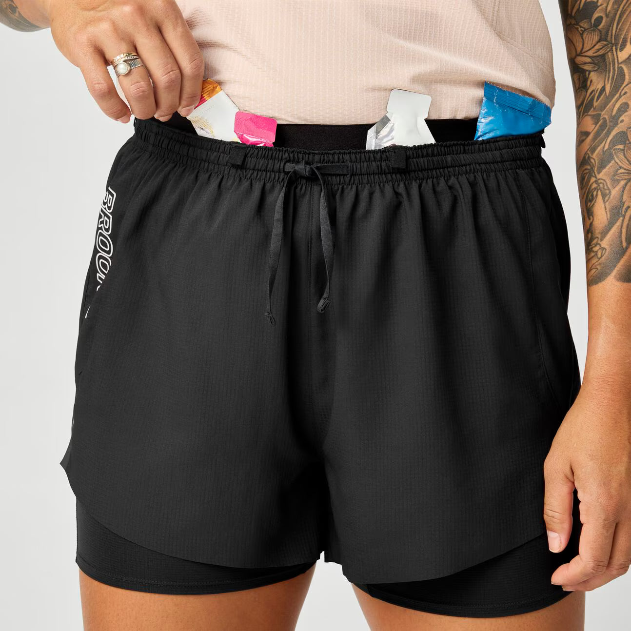 brooks cascadia 2-in-1 short, lightweight running short with pockets for women, black colour with white brooks logo, close up storage pocket filled with gels on brooks shorts on a white background