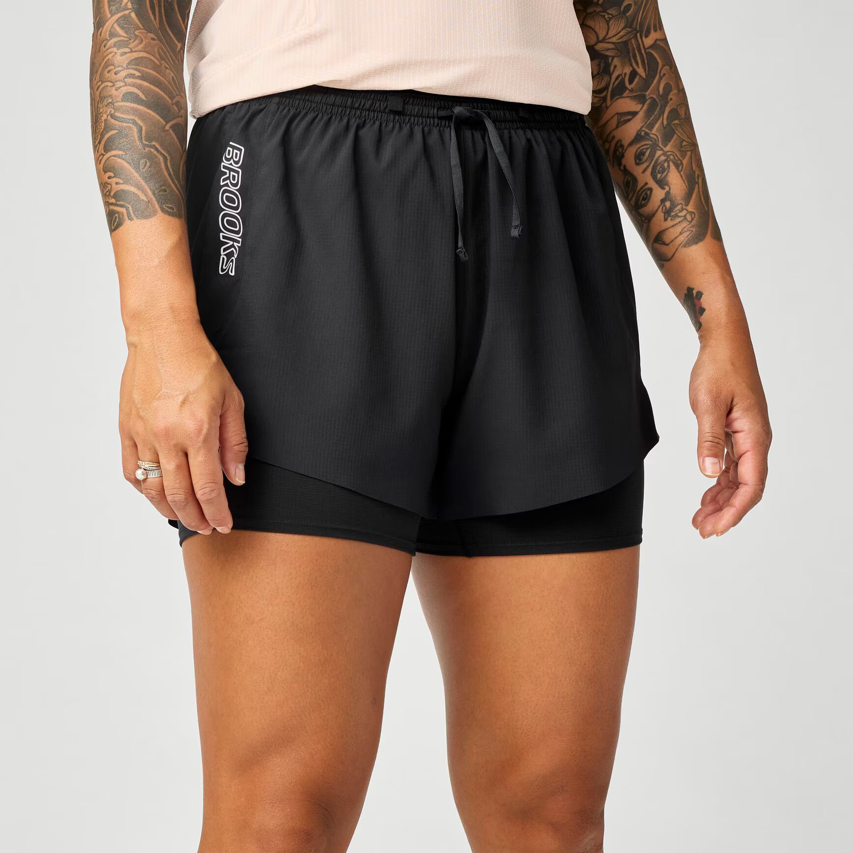 brooks cascadia 2-in-1 short, lightweight running short with pockets for women, black colour with white brooks logo, view of woman wearing brooks shorts on a white background