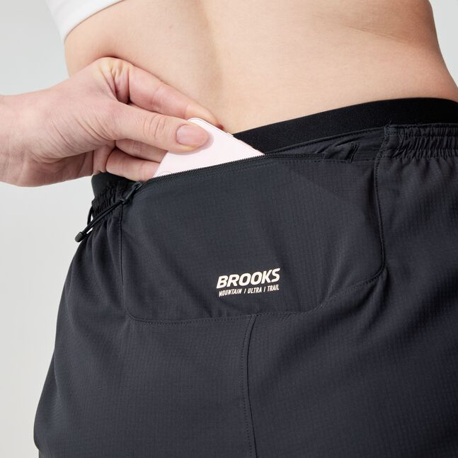 woman wearing brooks cascadia running short, lightweight women's trail-running shorts, black with white logo, close up of back pocket of short