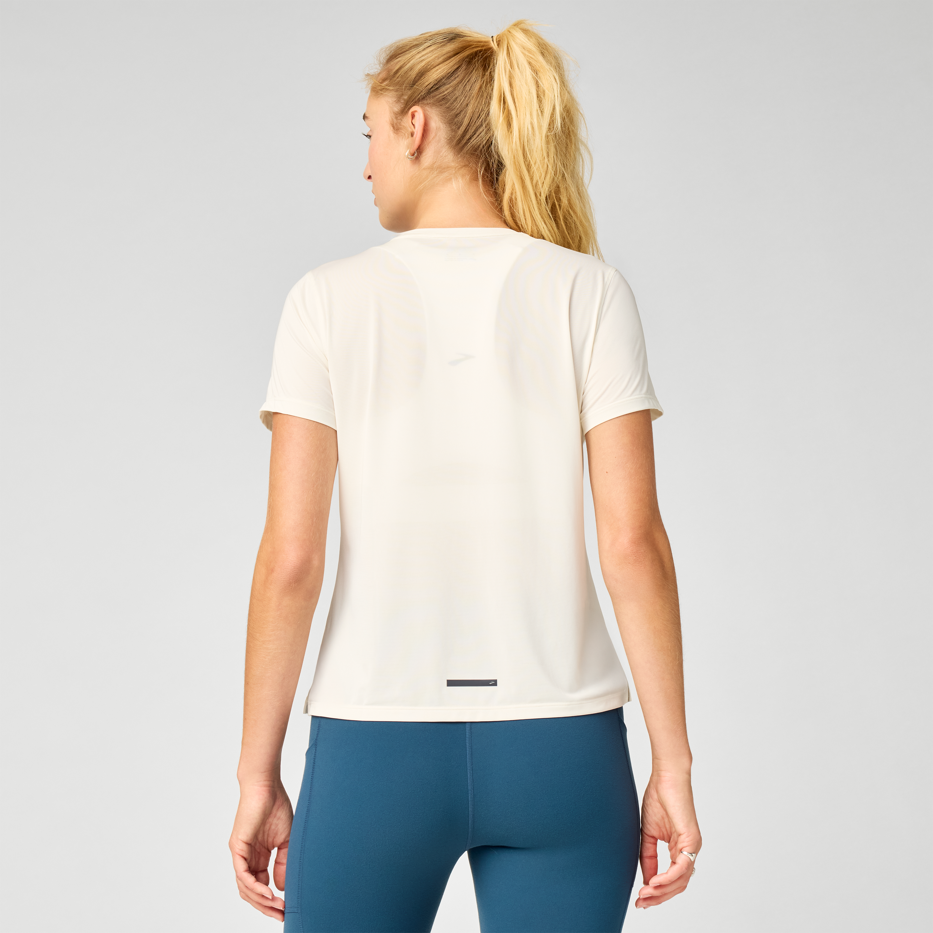 brooks womens dash reflective short sleeve, super lightweight and breathable running top, white colour with silver reflective logo, back of woman wearing tshirt with reflective stripe on bottom of top