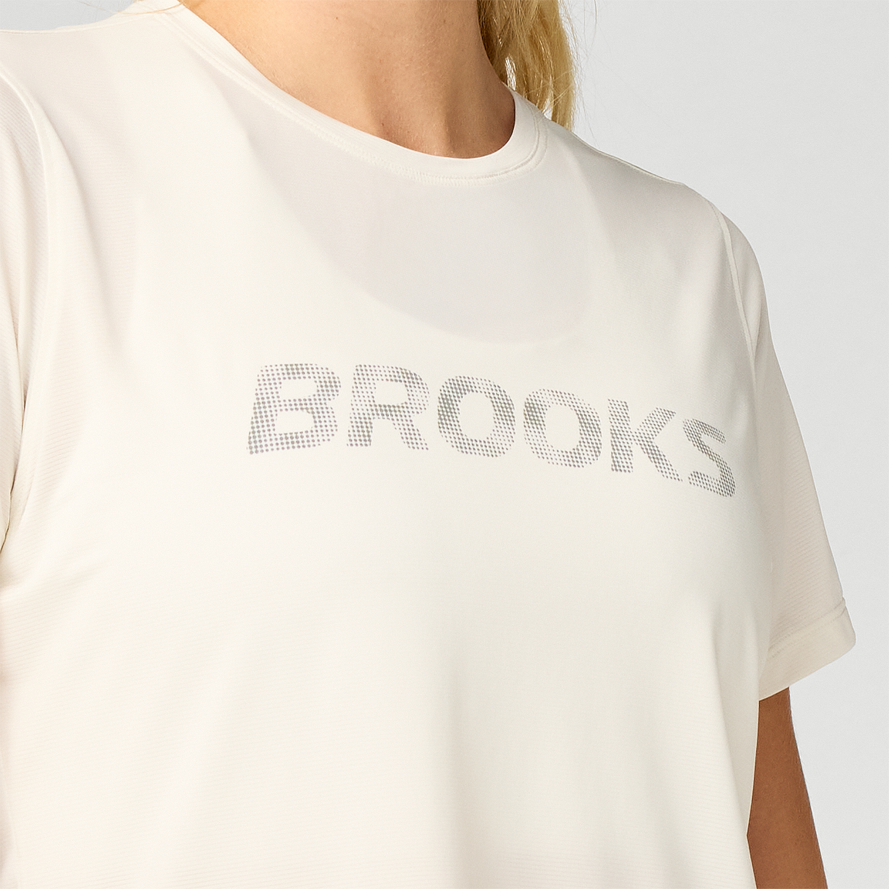 brooks womens dash reflective short sleeve, super lightweight and breathable running top, white colour with silver reflective logo, up close of tshirt chest and logo 