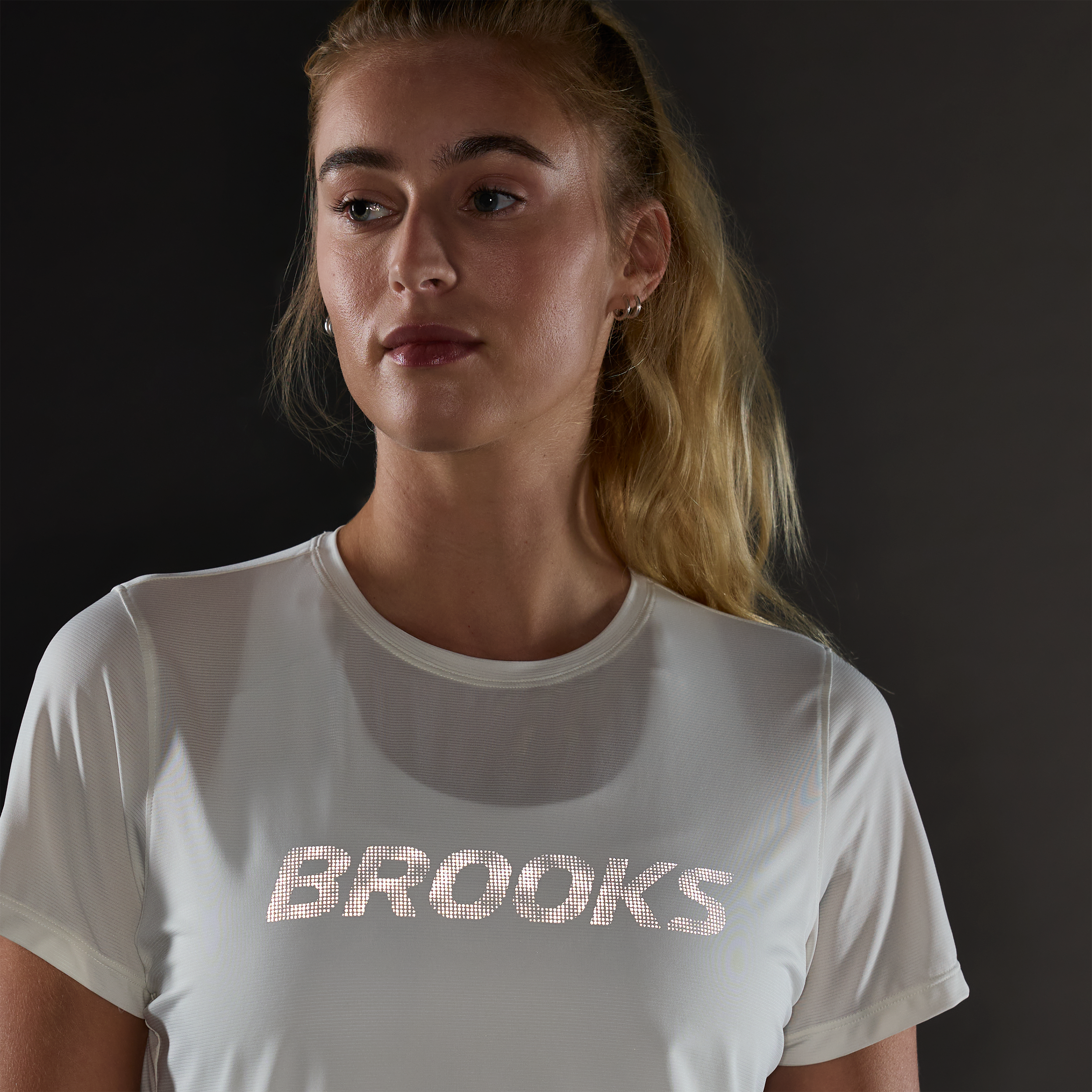 brooks womens dash reflective short sleeve, super lightweight and breathable running top, white colour with silver reflective logo, woman wearing tshirt in dark with reflective logo lighting up