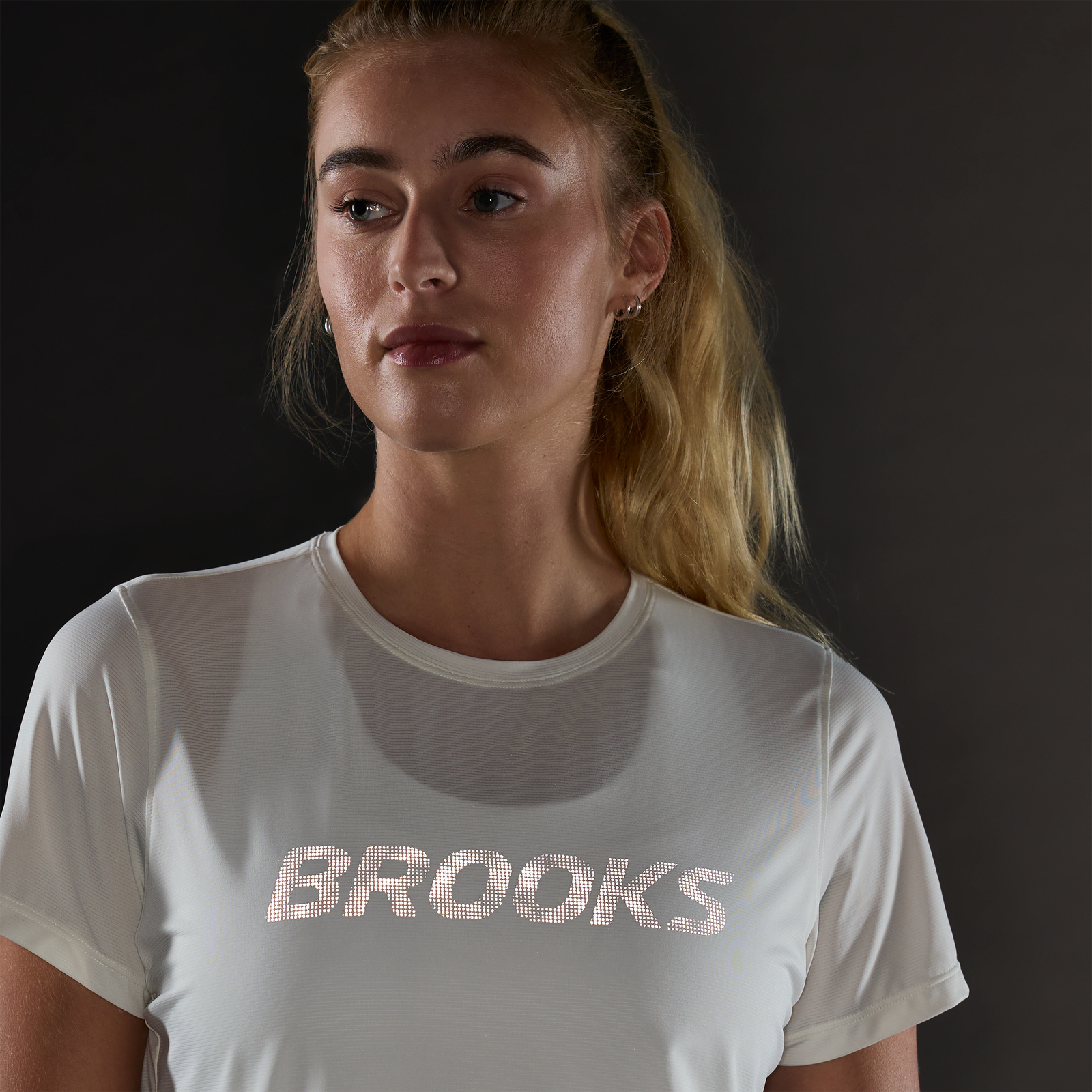 brooks womens dash reflective short sleeve, super lightweight and breathable running top, white colour with silver reflective logo, woman wearing tshirt in dark with reflective logo lighting up