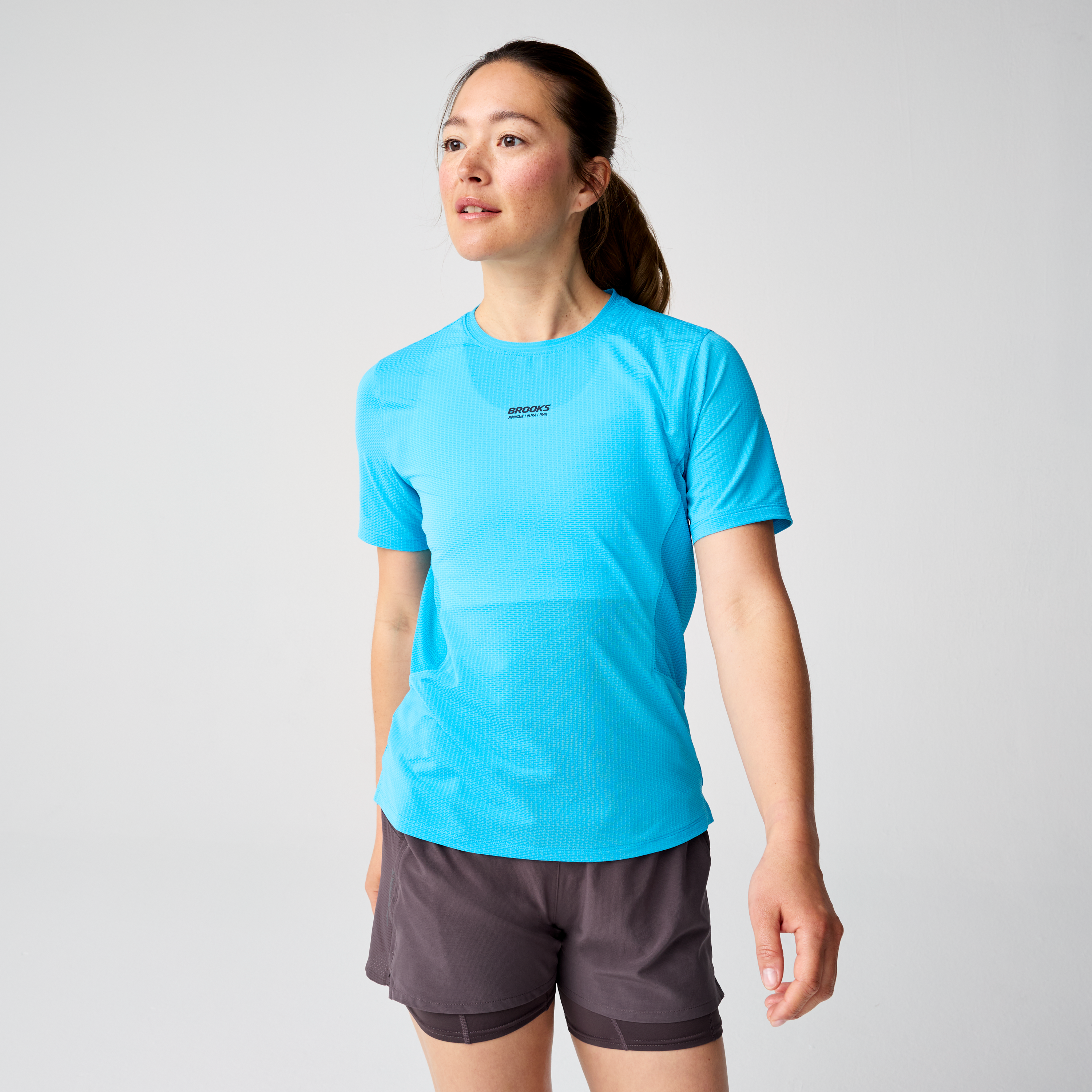 brooks womens high point short sleeve 2.0, super lightweight and breathable trail running top, bright blue colour, woman wearing brooks top with grey background