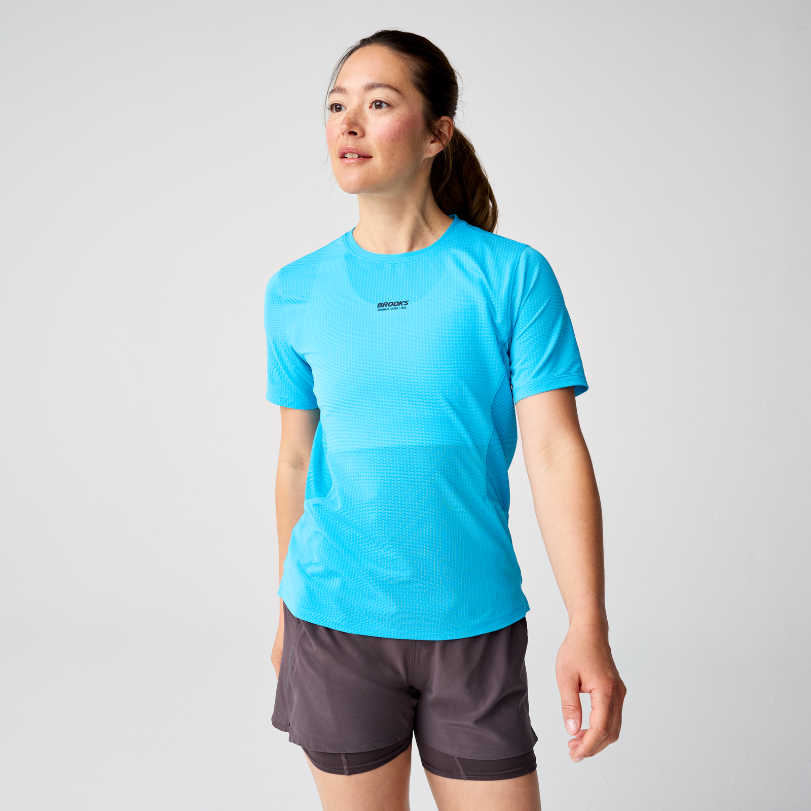 brooks womens high point short sleeve 2.0, super lightweight and breathable trail running top, bright blue colour, woman wearing brooks top with grey background