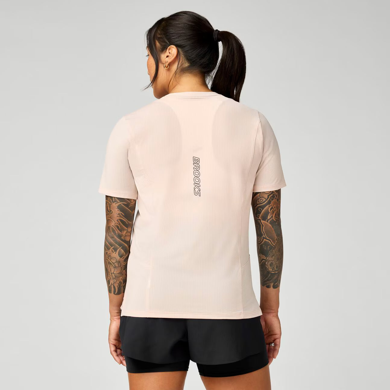 brooks womens high point short sleeve 2.0, super lightweight and breathable trail running top, light pink colour, woman wearing brooks top with grey background